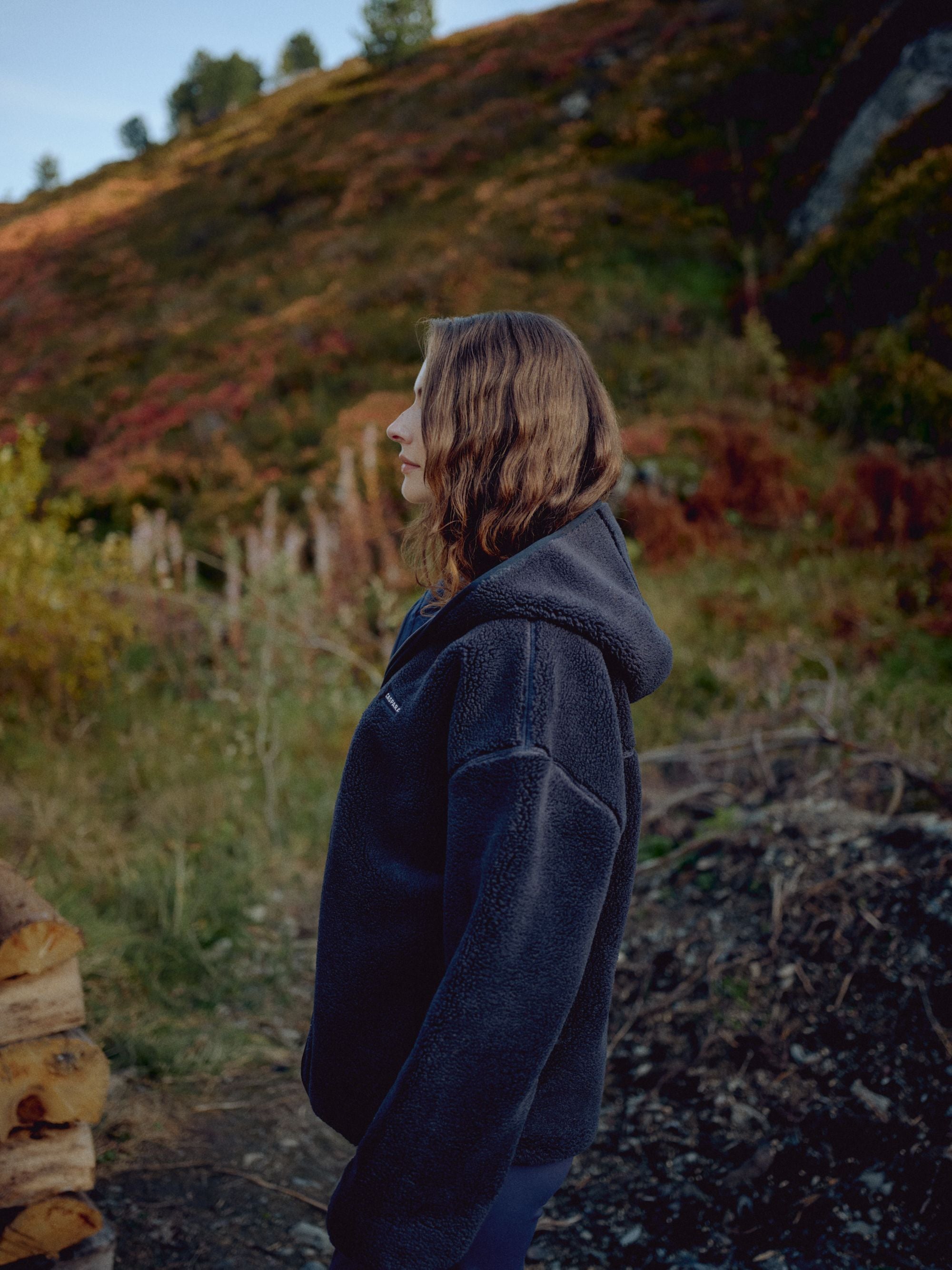 Woman wearing a navy CASPARA Cloudfleece hooded jacket standing outdoors on a hillside.