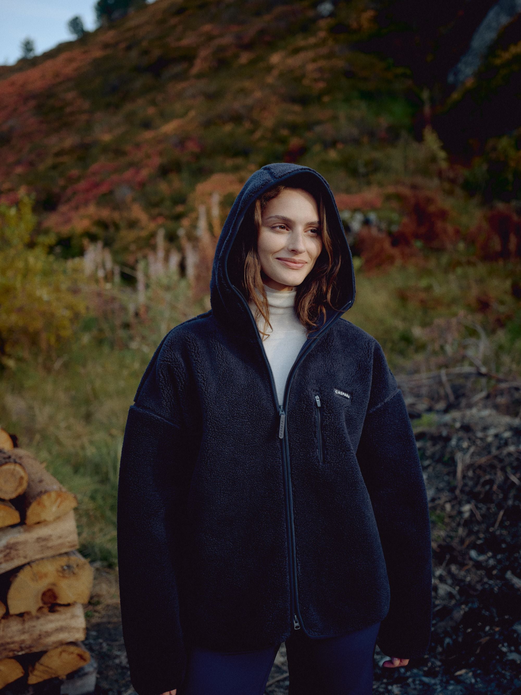 Woman wearing a navy CASPARA Cloudfleece hooded jacket in an autumn landscape.