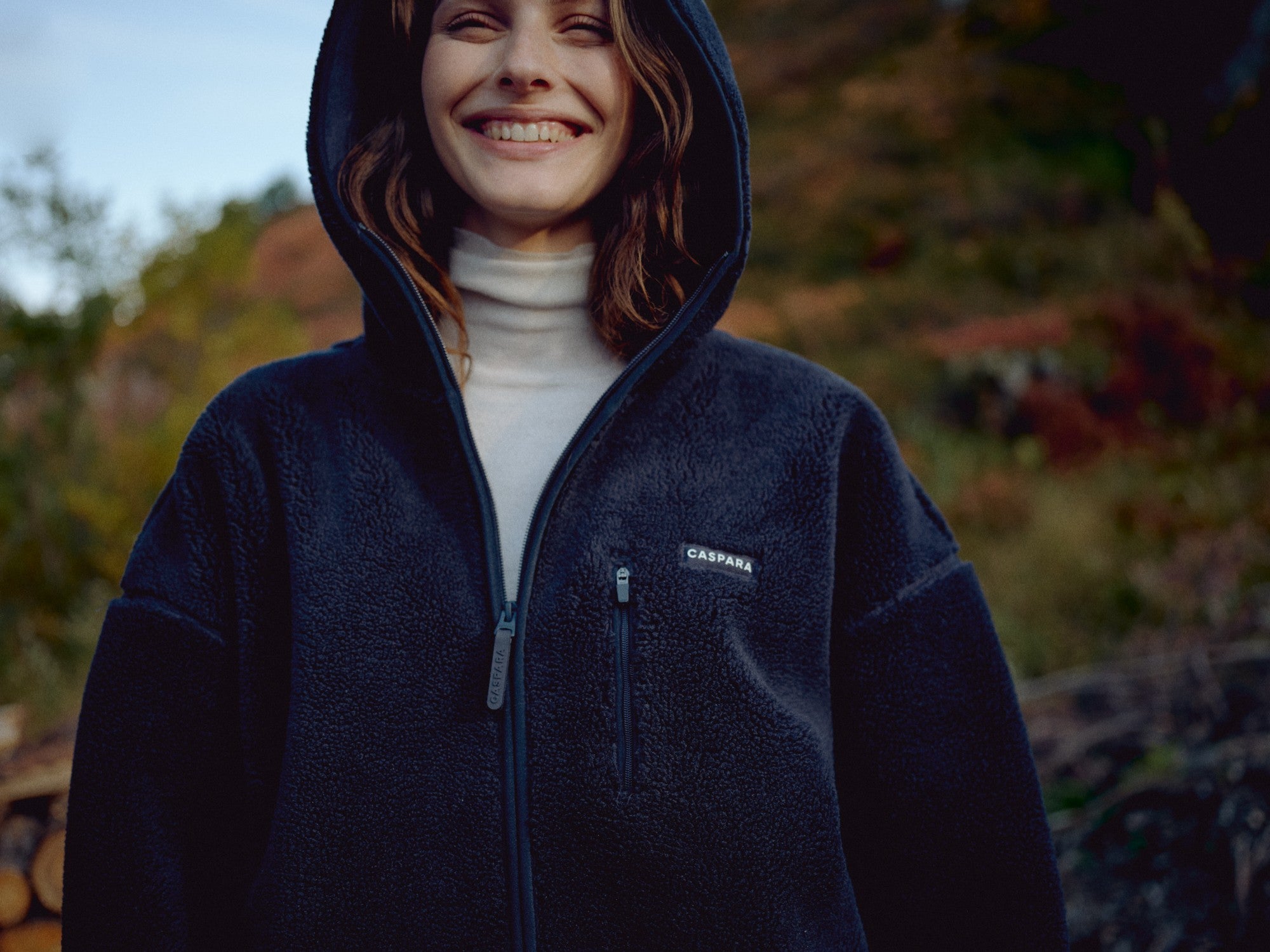 Woman smiling outdoors wearing a navy CASPARA Cloudfleece hooded jacket.