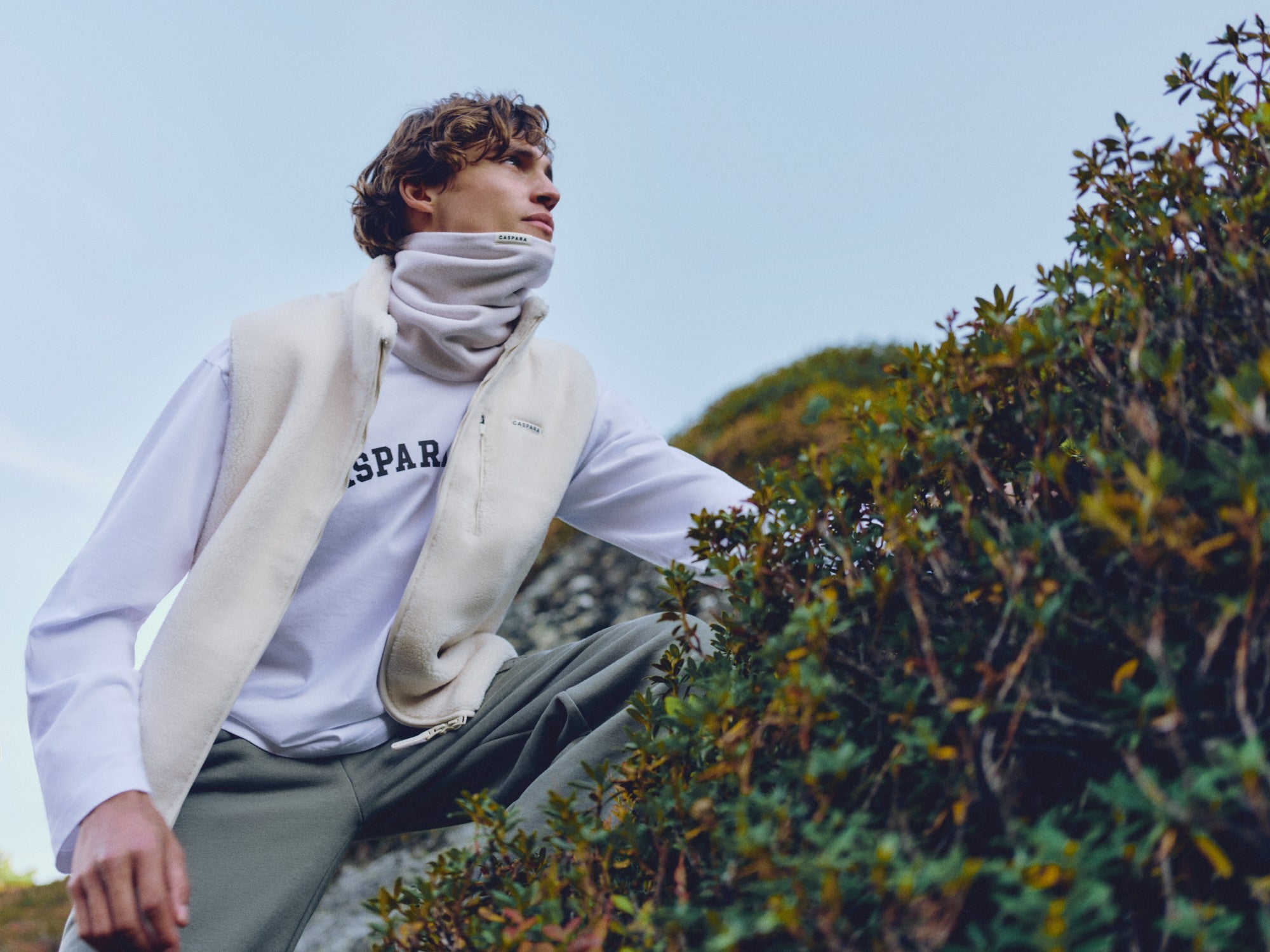 Man wearing a creme CASPARA Cloudfleece vest outdoors on a hillside.