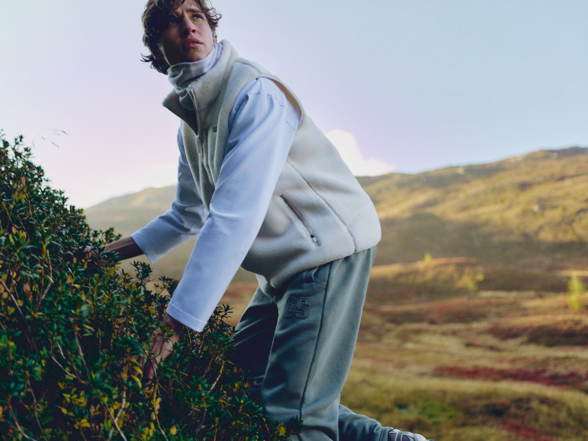Man wearing a creme CASPARA Cloudfleece vest on a mountain hillside.