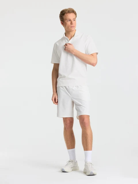 Man wearing white CASPARA Prime Core shorts and a matching polo shirt in a studio.