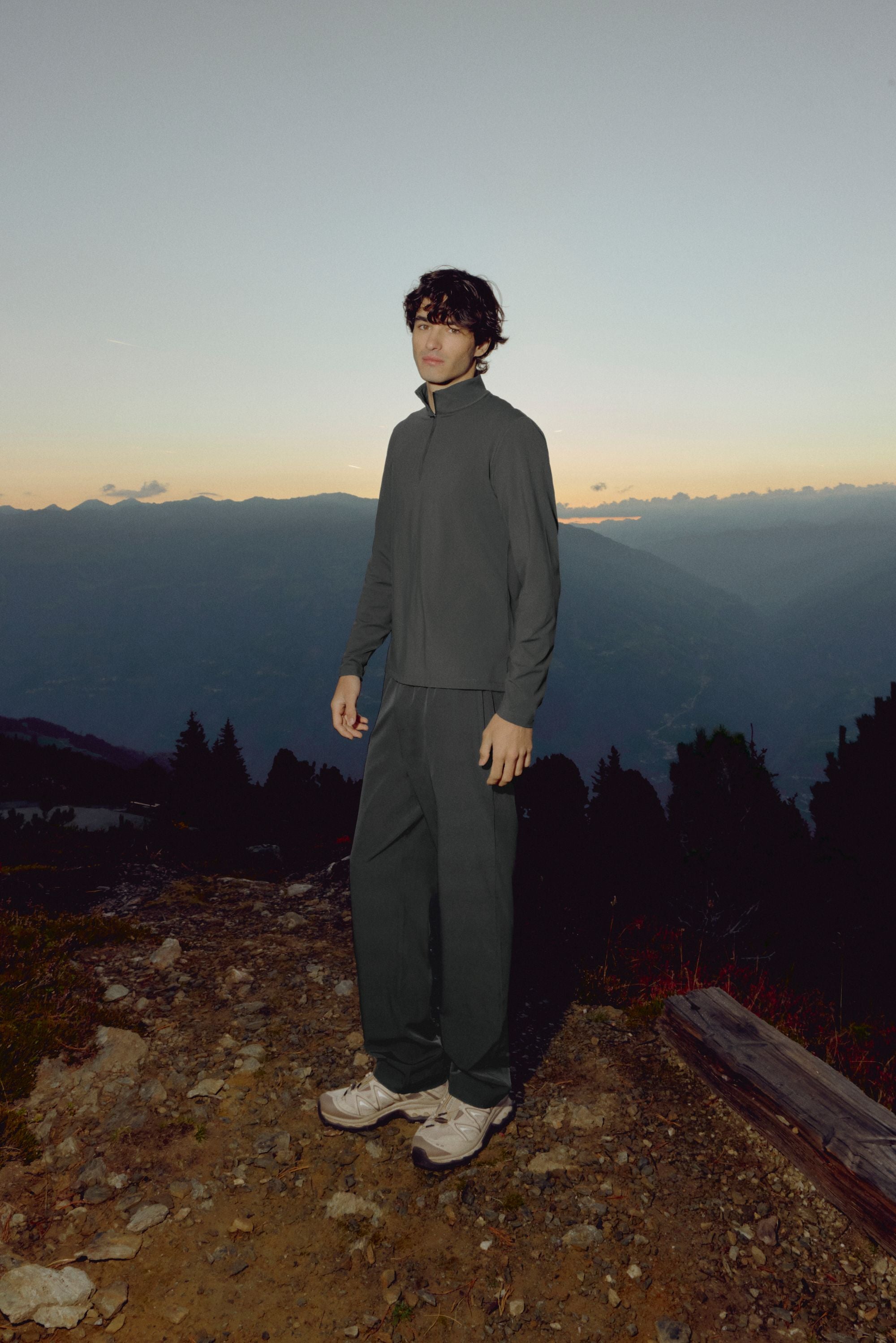 Man wearing olive green CASPARA Prime Core pants in a mountain landscape at dusk.