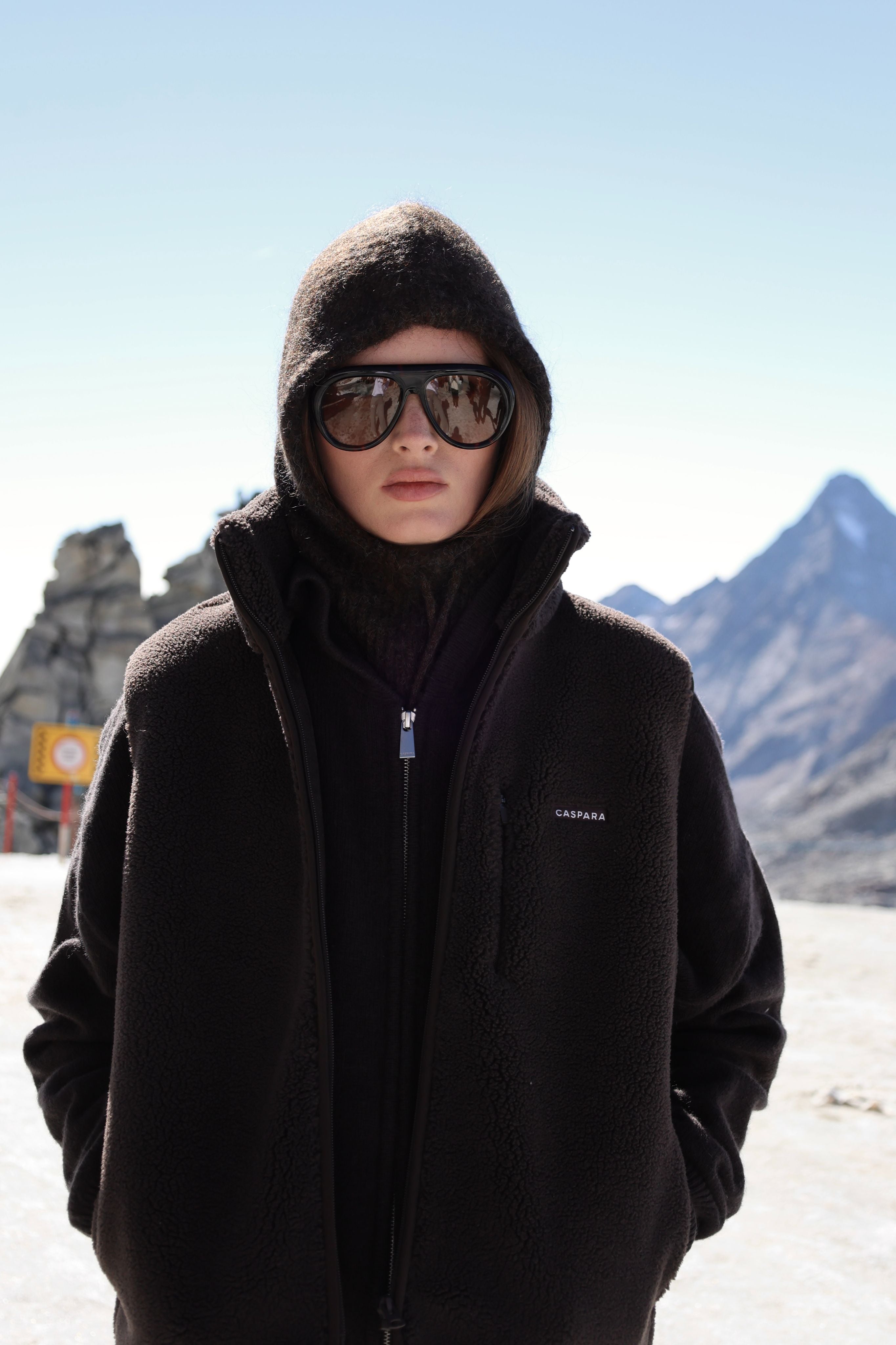 Woman wearing an espresso CASPARA Cloudfleece vest in a mountain setting.