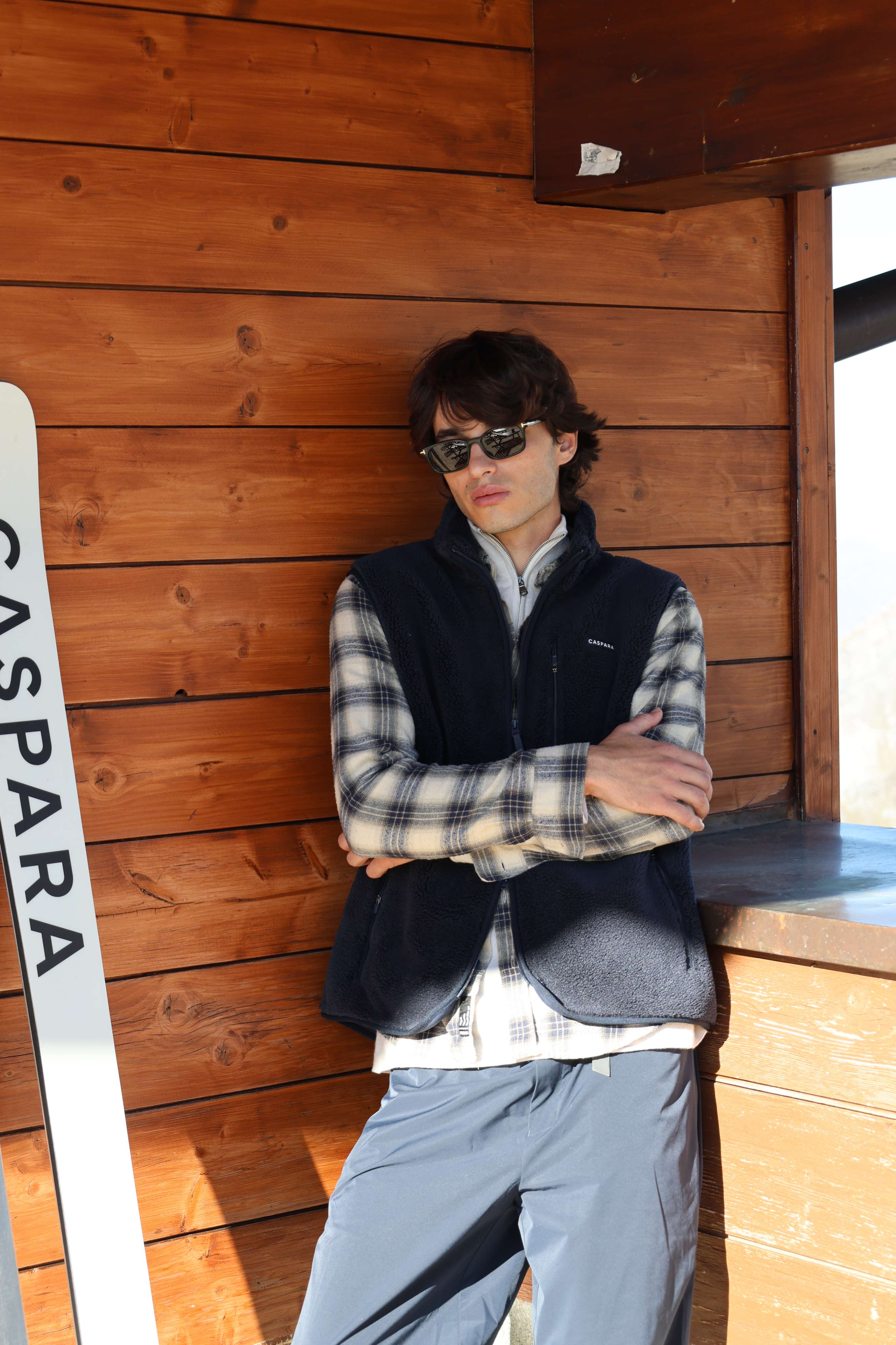 Man wearing a navy CASPARA Cloudfleece vest layered over a plaid shirt outdoors.