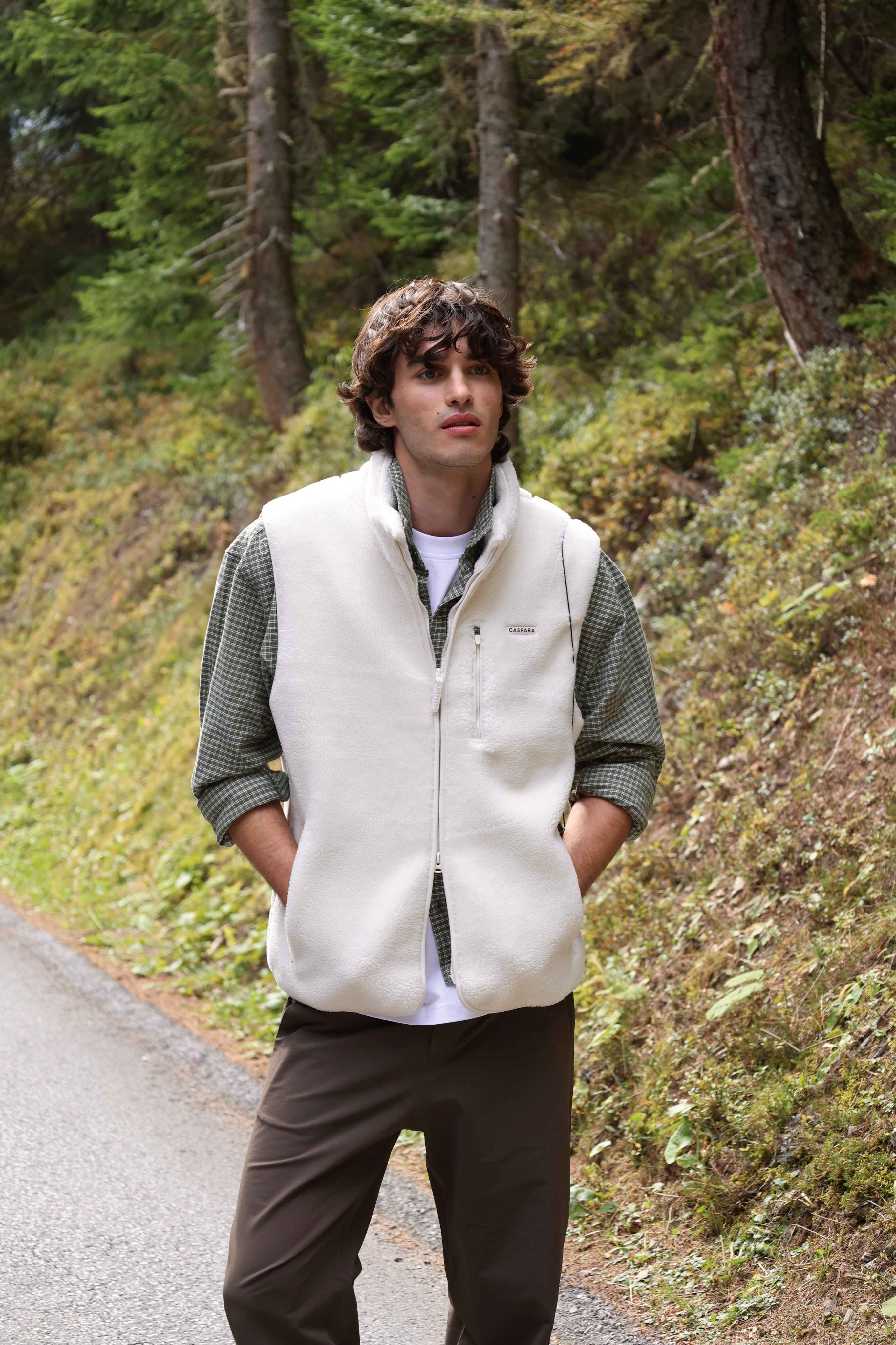 Man wearing a creme CASPARA fleece vest outdoors on a forest path.