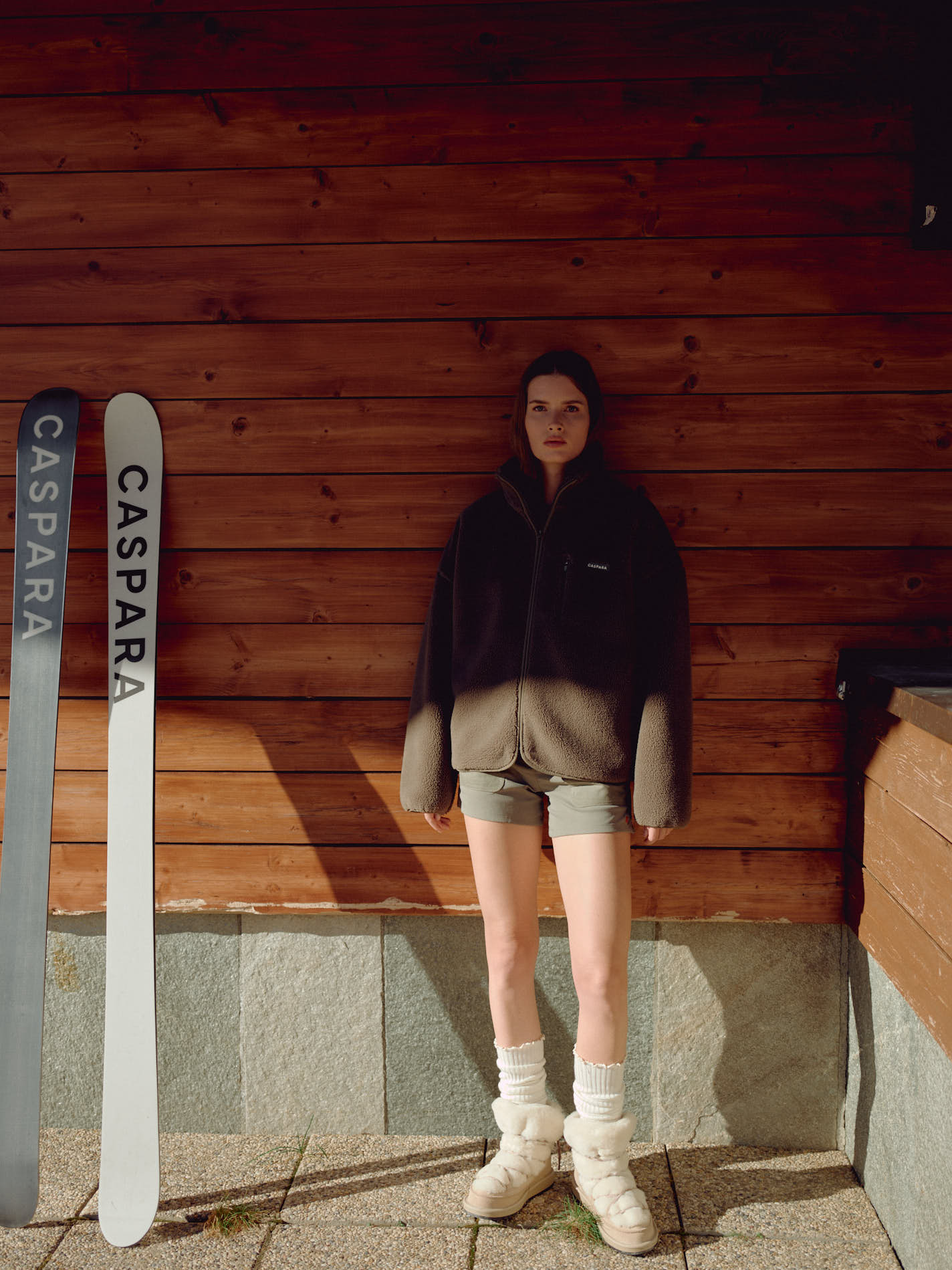 Woman wearing a khaki CASPARA Cloudfleece jacket standing outdoors next to skis.