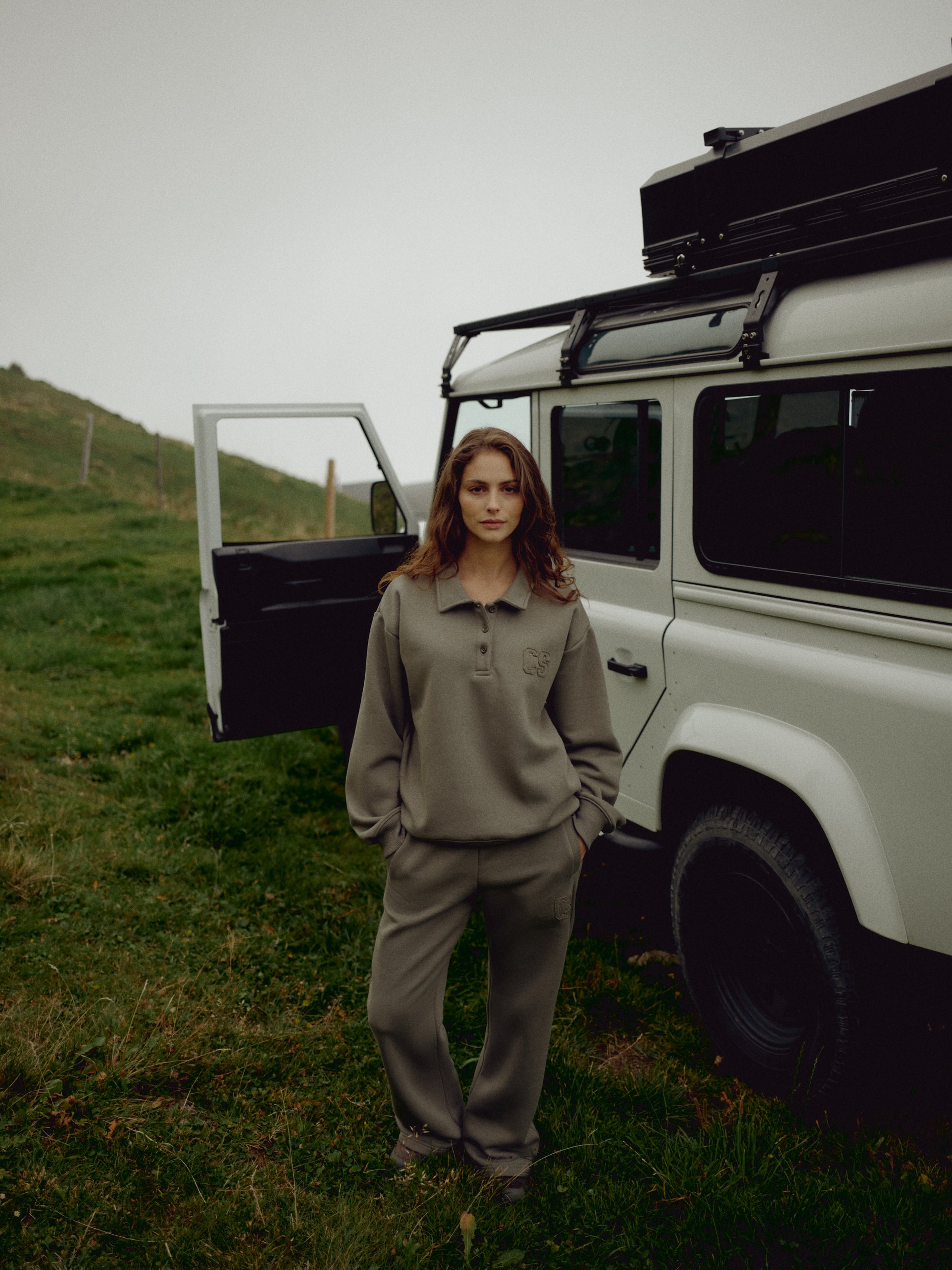 Woman wearing a khaki CASPARA CS rugby shirt next to an off-road vehicle.