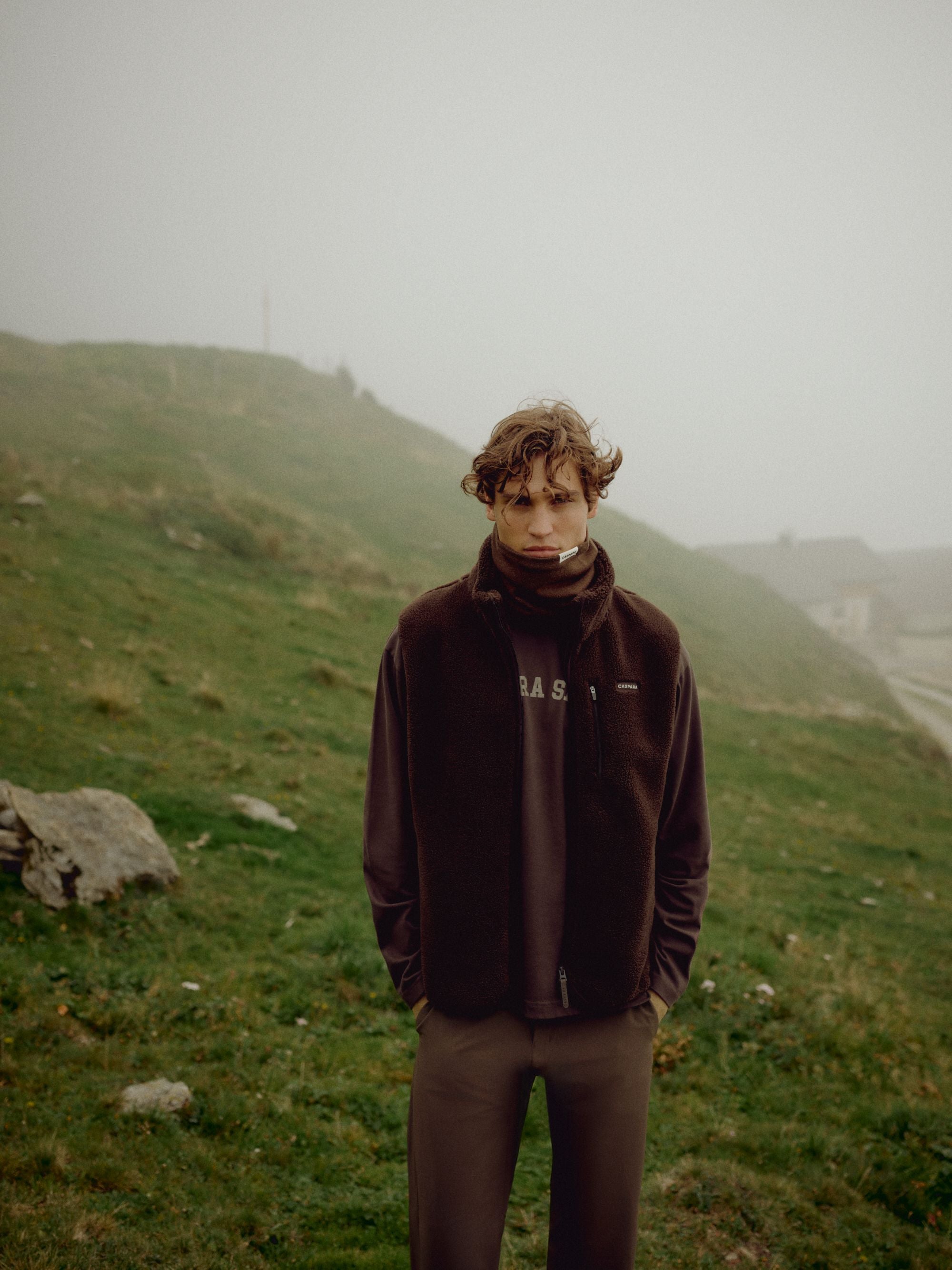 Man wearing an espresso CASPARA Cloudfleece vest on a misty hillside.