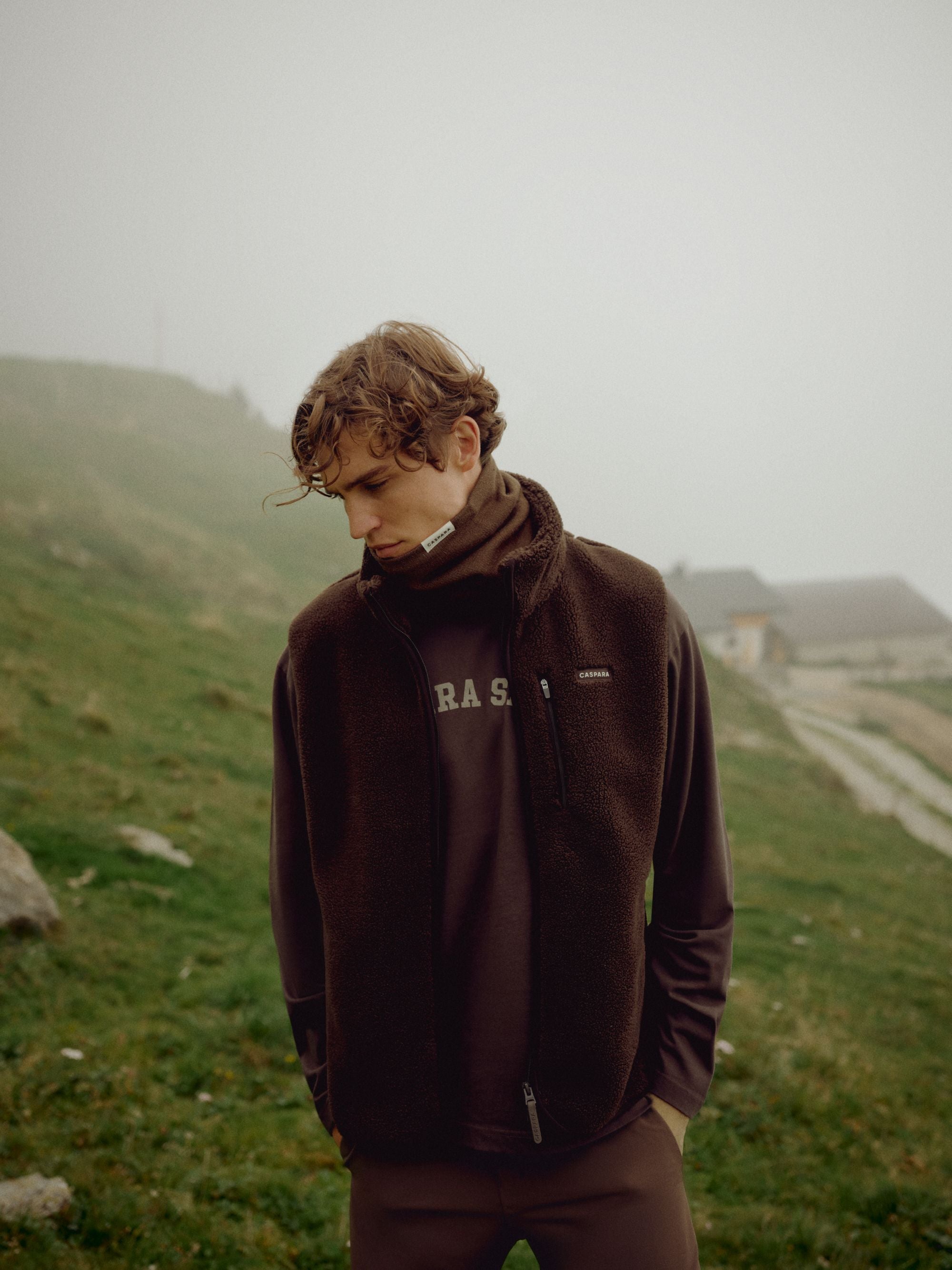 Man wearing an espresso CASPARA Cloudfleece vest on a misty mountain slope.