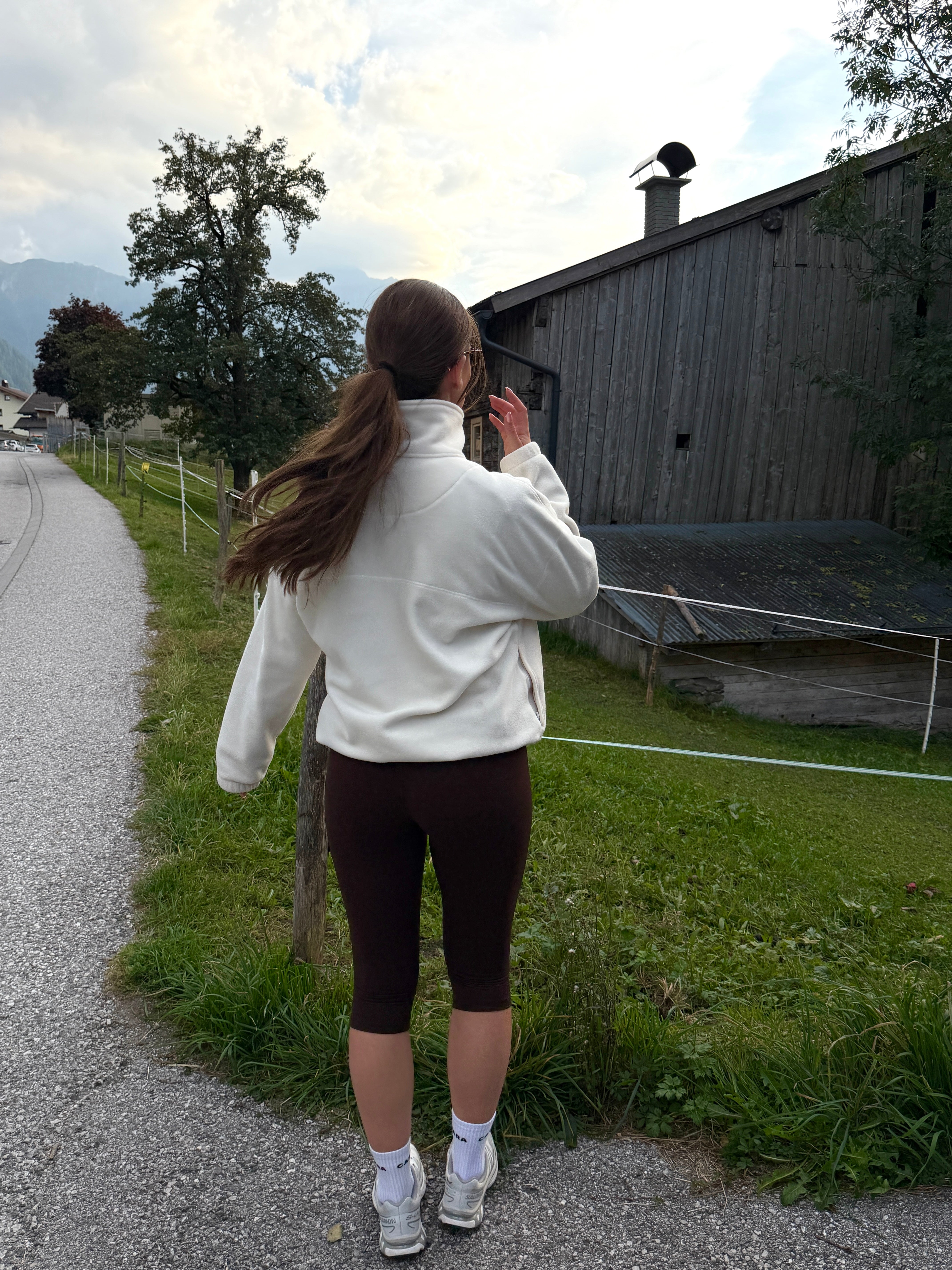 Woman wearing espresso CASPARA Cloudform capri leggings and a white fleece jacket walking outdoors.