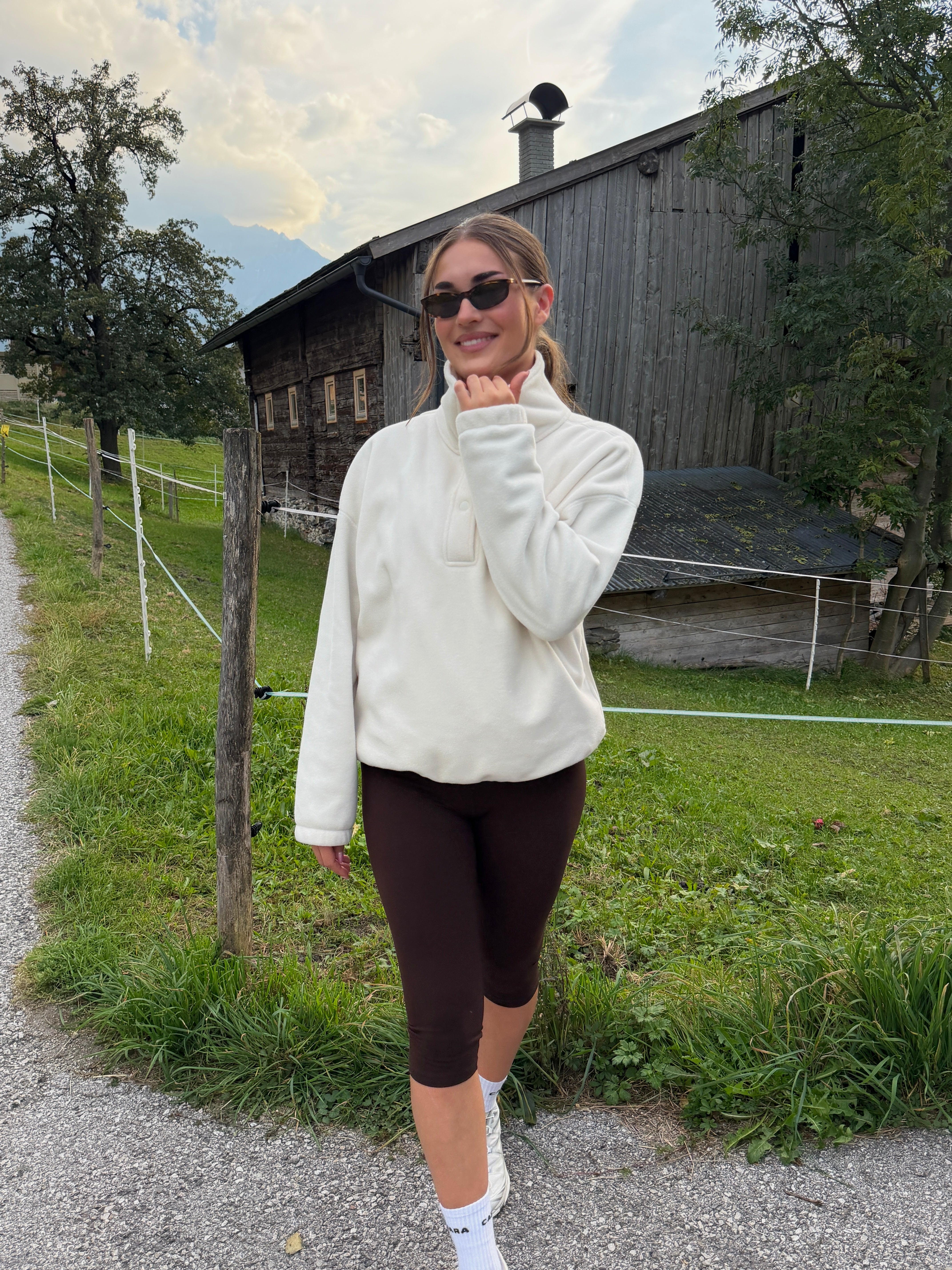 Woman wearing espresso CASPARA Cloudform capri leggings and a white fleece near a wooden barn.