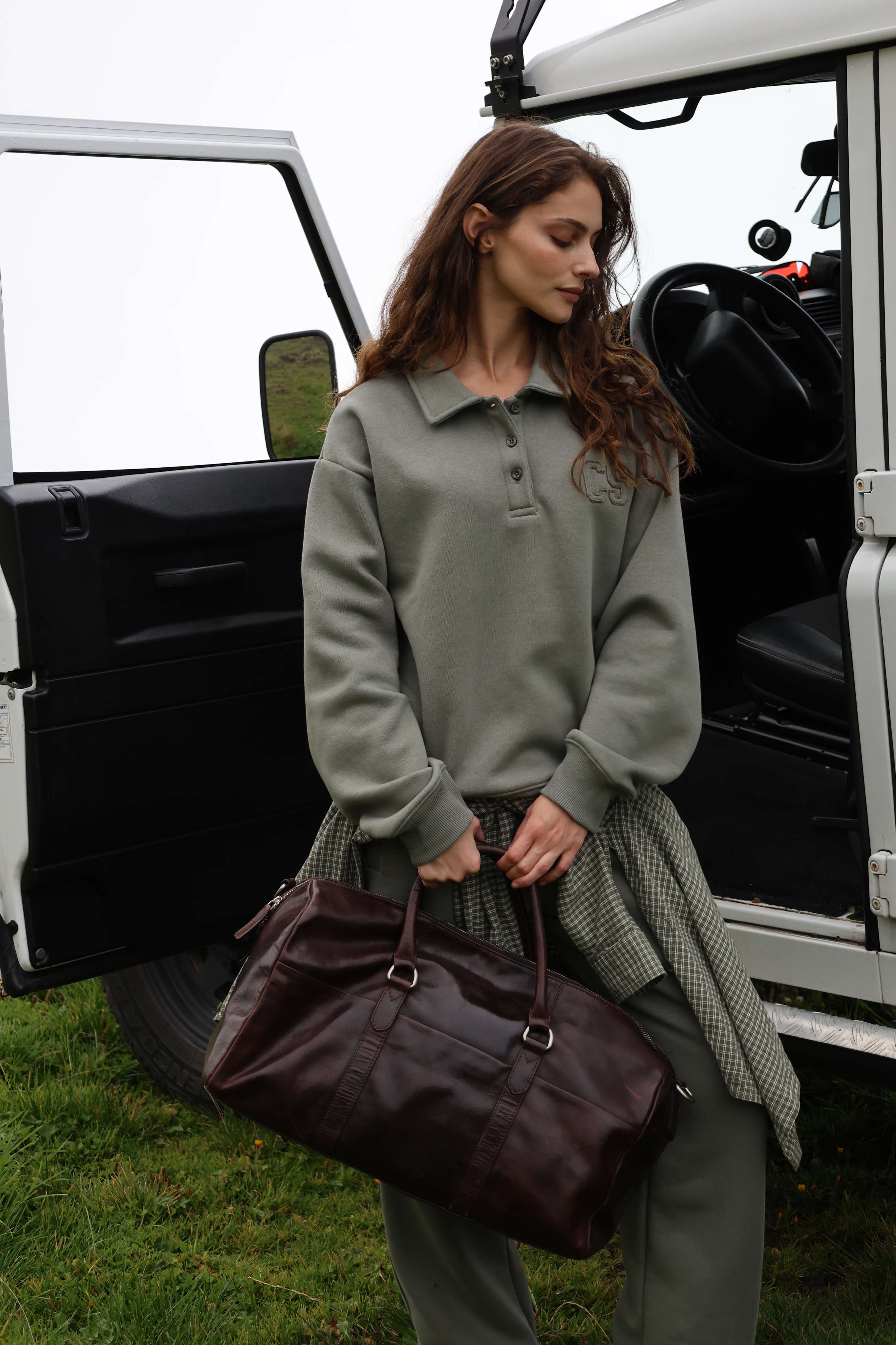 Woman wearing a khaki CASPARA CS rugby shirt and matching sweatpants by an open car door.