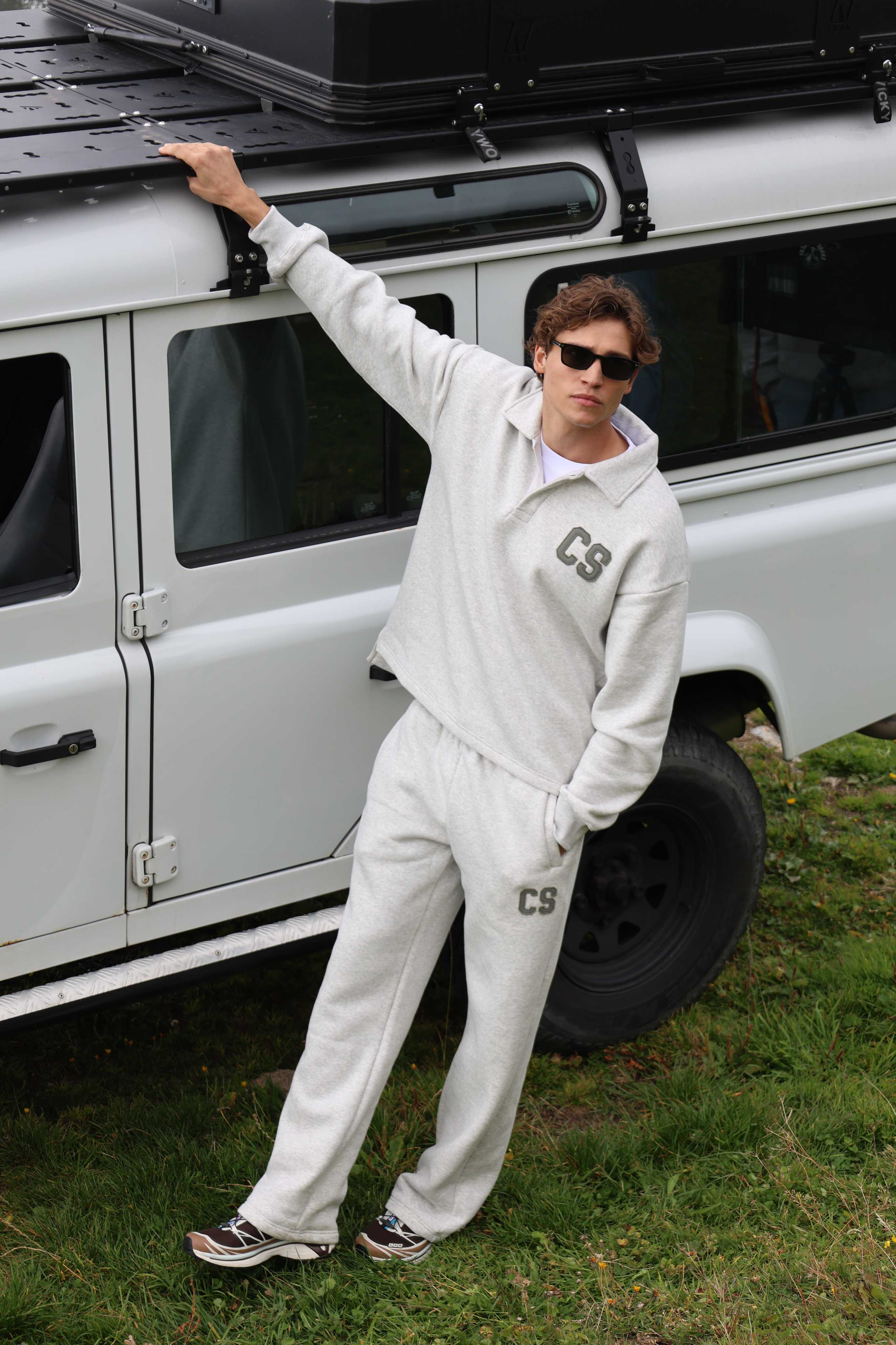 Man wearing a grey melange CASPARA CS rugby shirt leaning against an off-road vehicle.