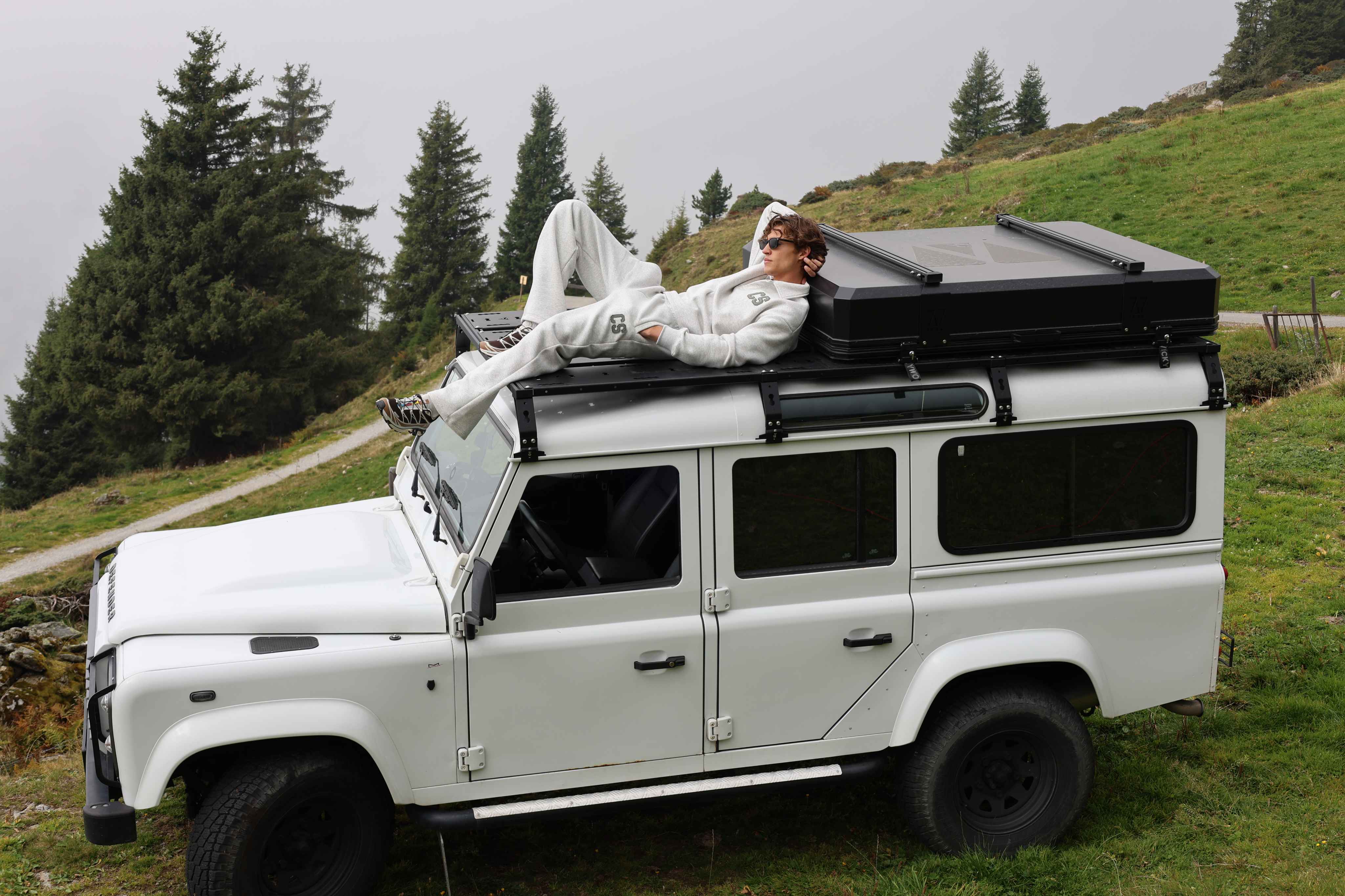 Man wearing a grey melange CASPARA CS rugby shirt and sweatpants on a car roof.