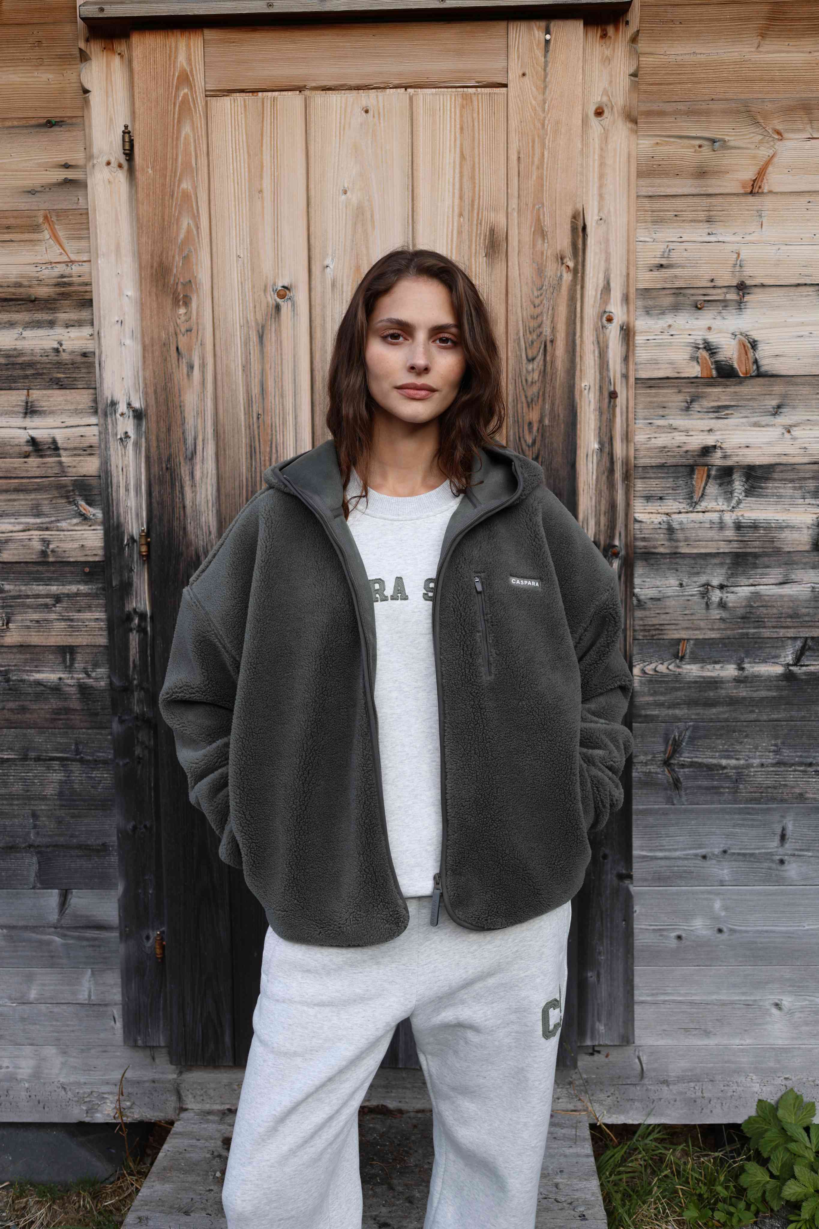 Woman wearing a grey melange CASPARA CS crewneck and fleece jacket in front of a wooden door.