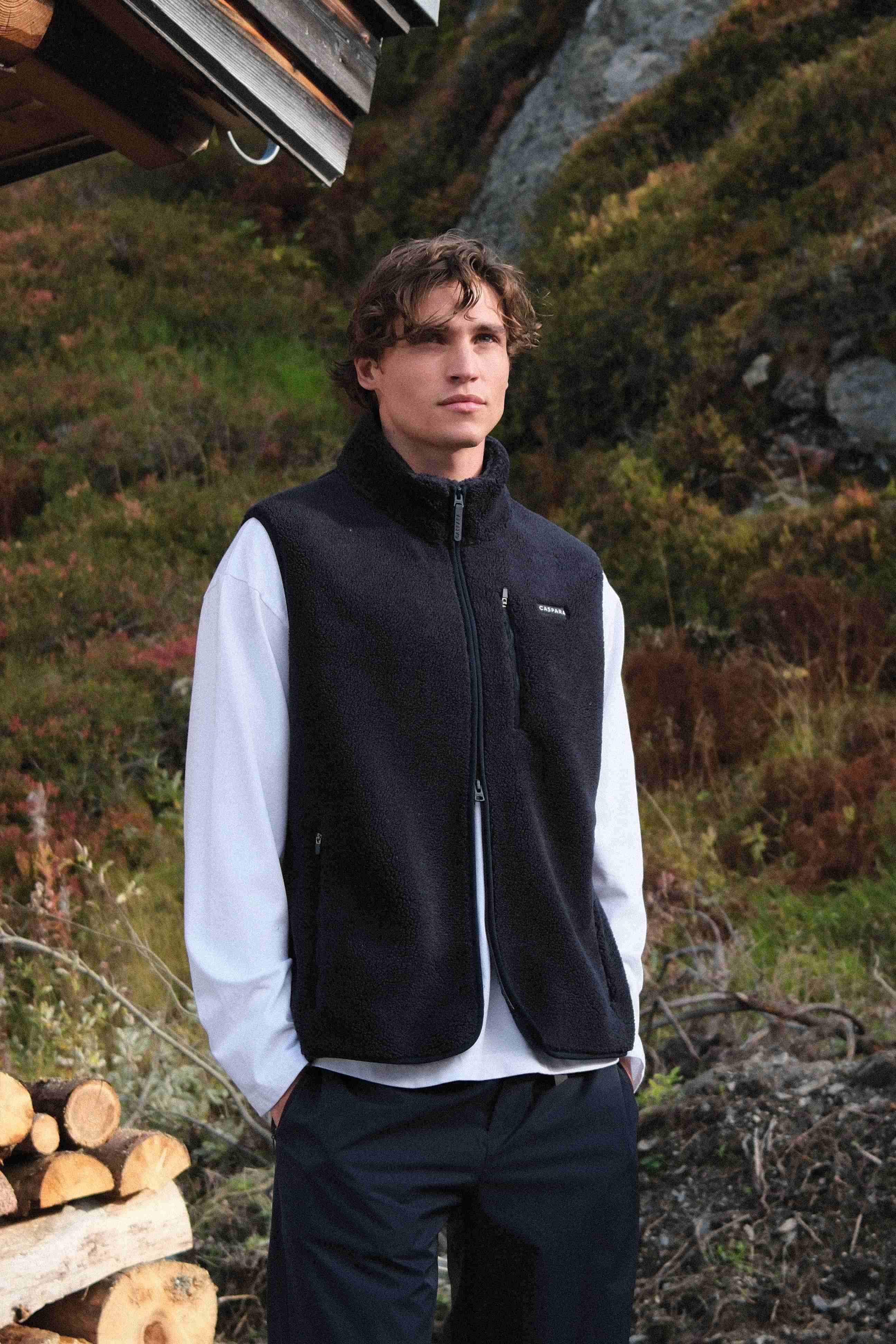 Man wearing a navy CASPARA Cloudfleece vest over a white long-sleeve shirt outdoors.