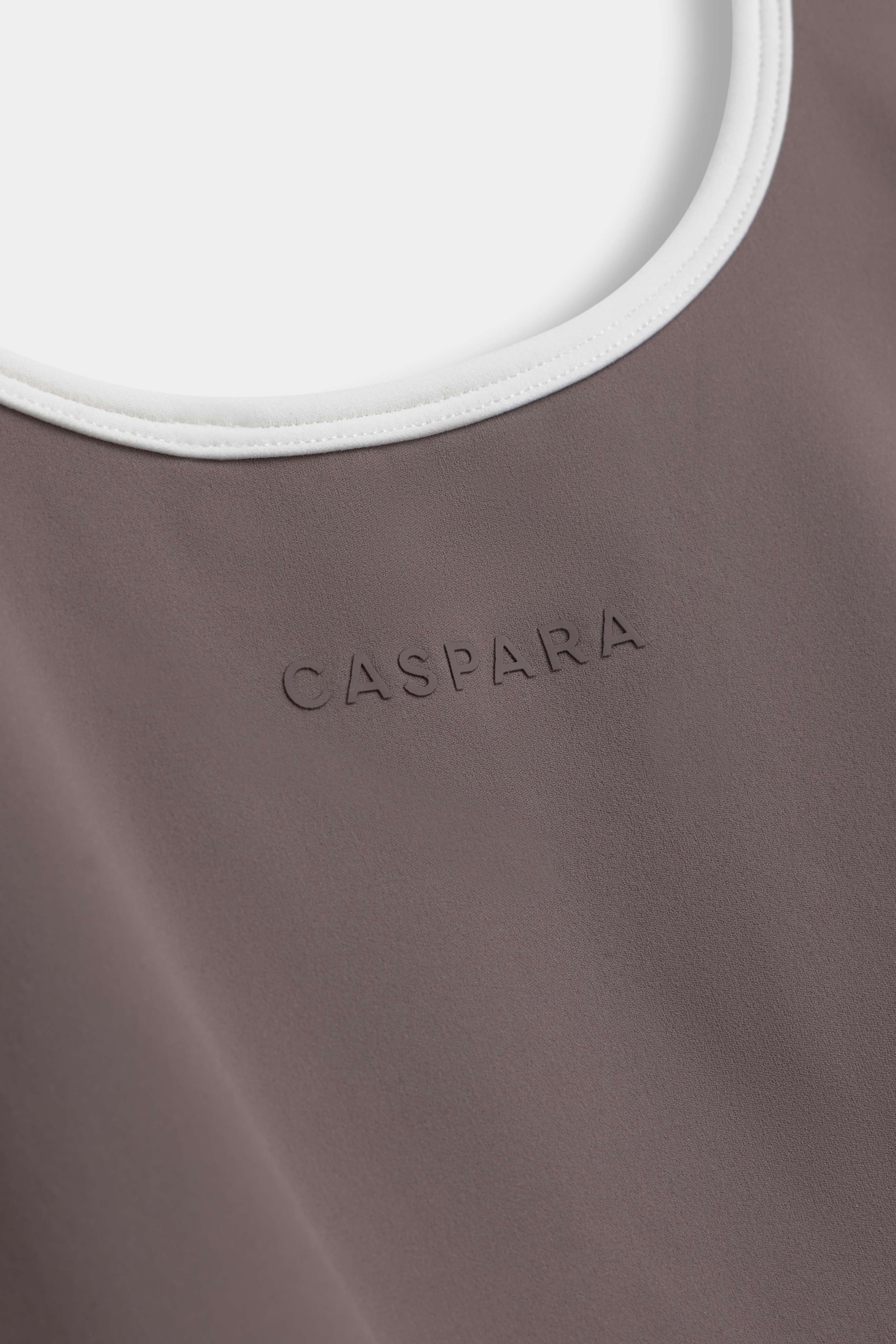 Close-up of the CASPARA Cloudform top in walnut with white neckline trim and embossed logo.