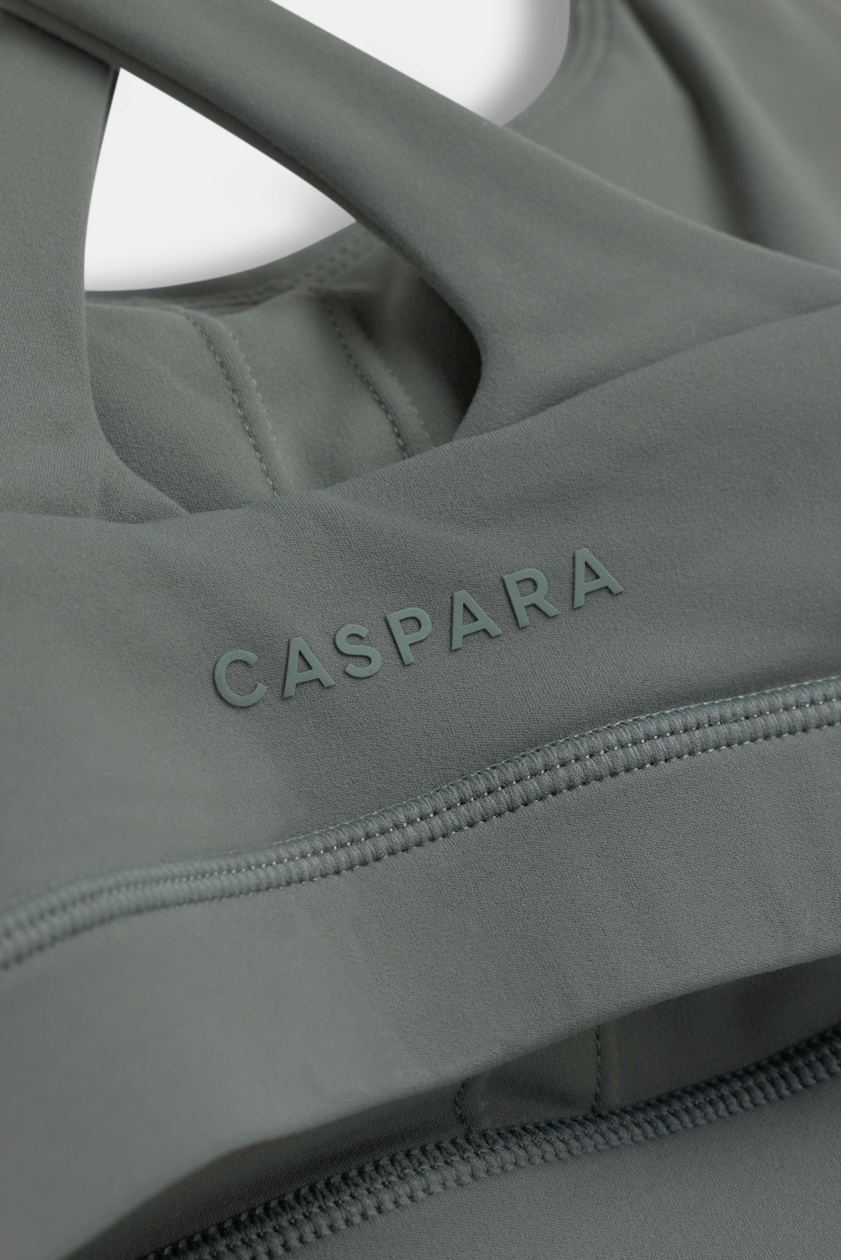 Close-up of the khaki CASPARA Cloudform crossback sports bra showing the embossed logo and seams.