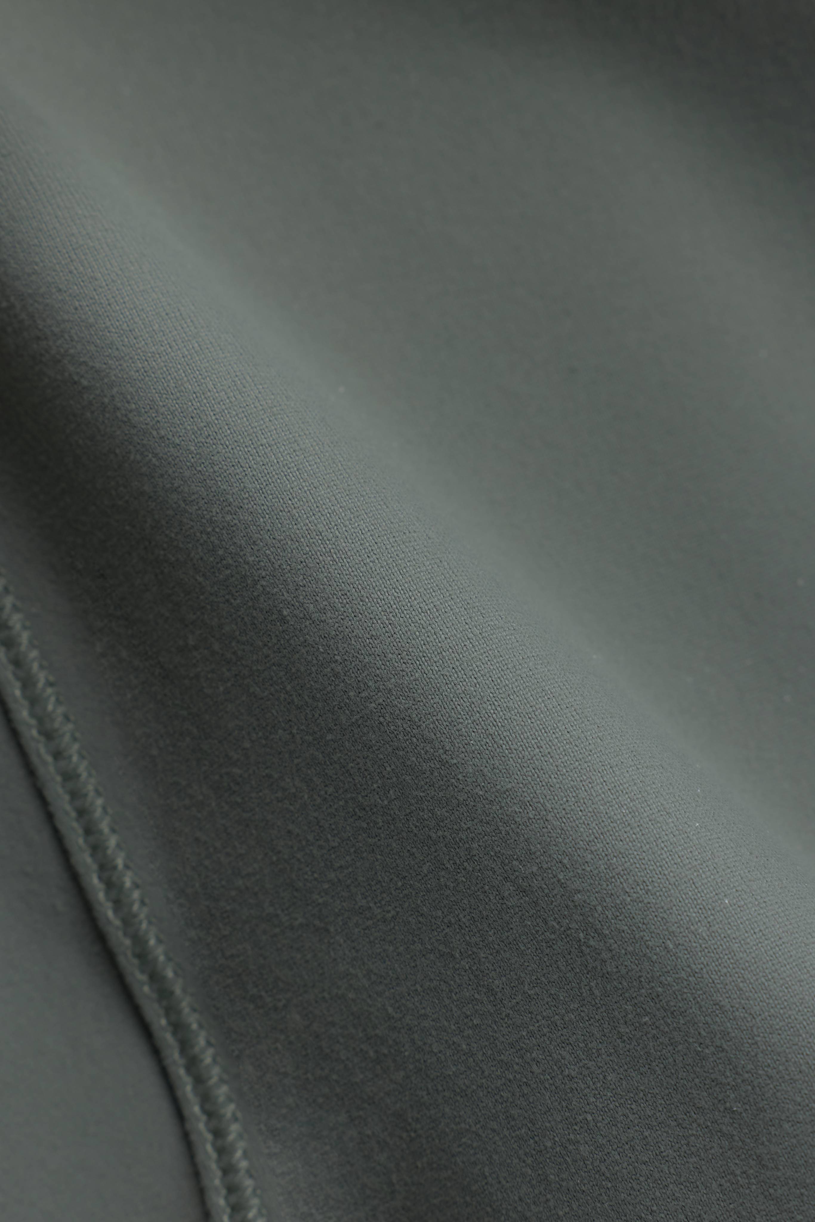 Close-up of the smooth khaki fabric and stitched seam on the CASPARA Sculptluxe zip jacket.