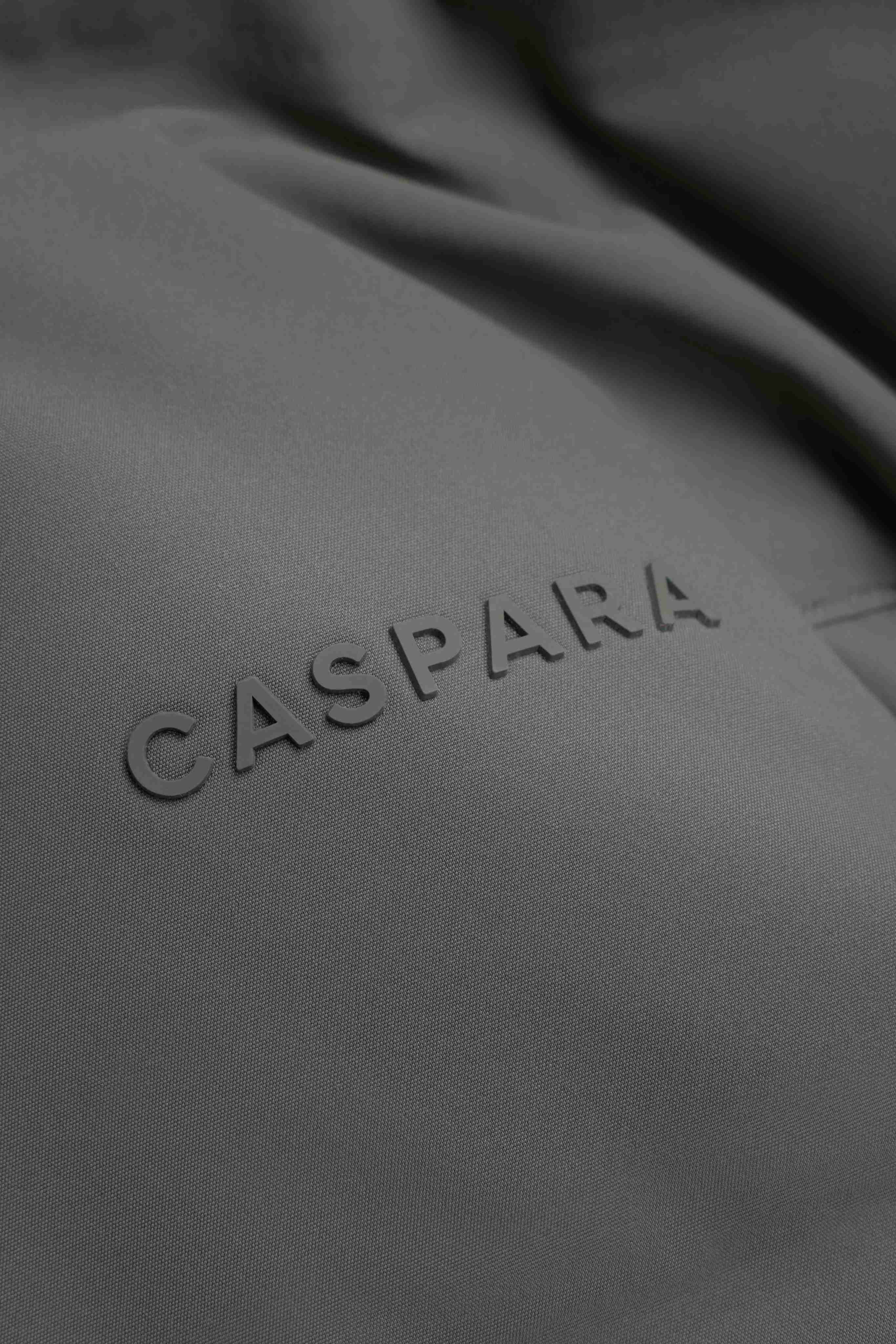 Close-up of the embossed CASPARA logo on the khaki Boreal Puffer Jacket.