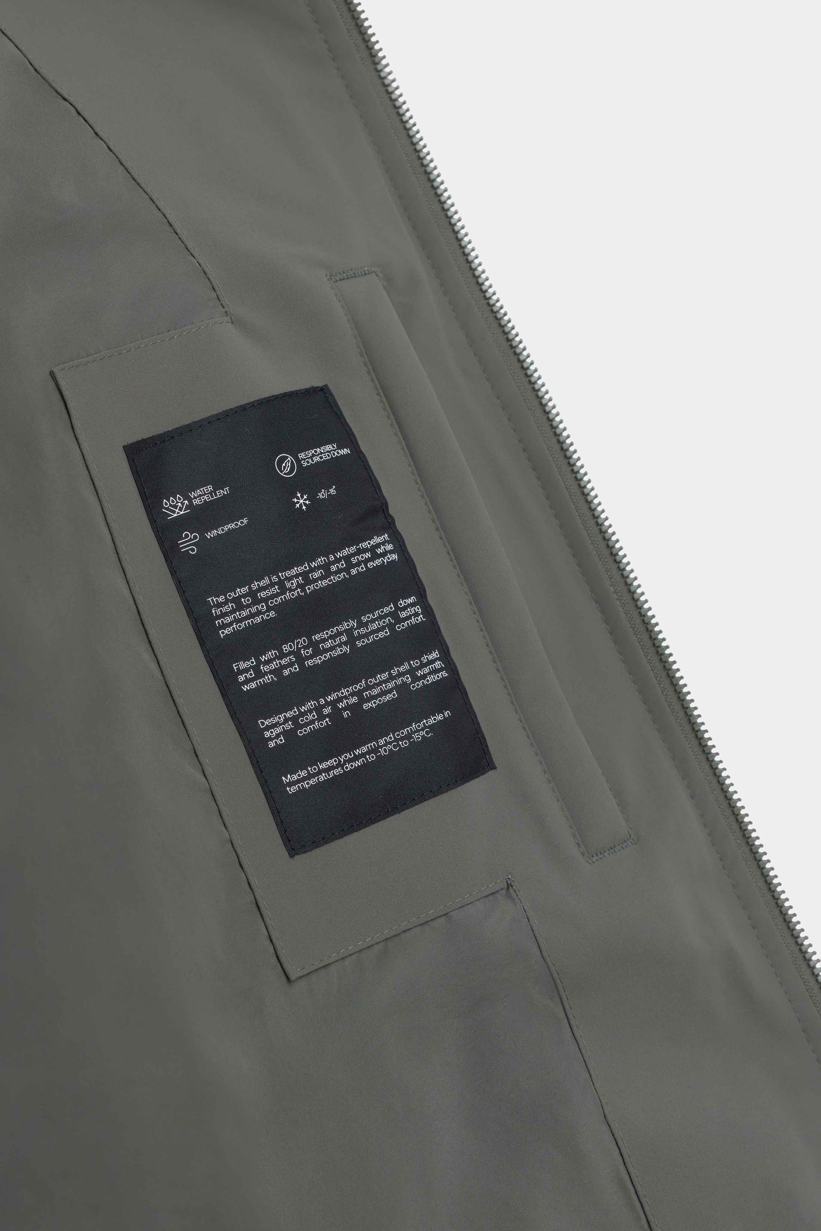 Close-up of the interior feature label on the khaki CASPARA Boreal puffer jacket.