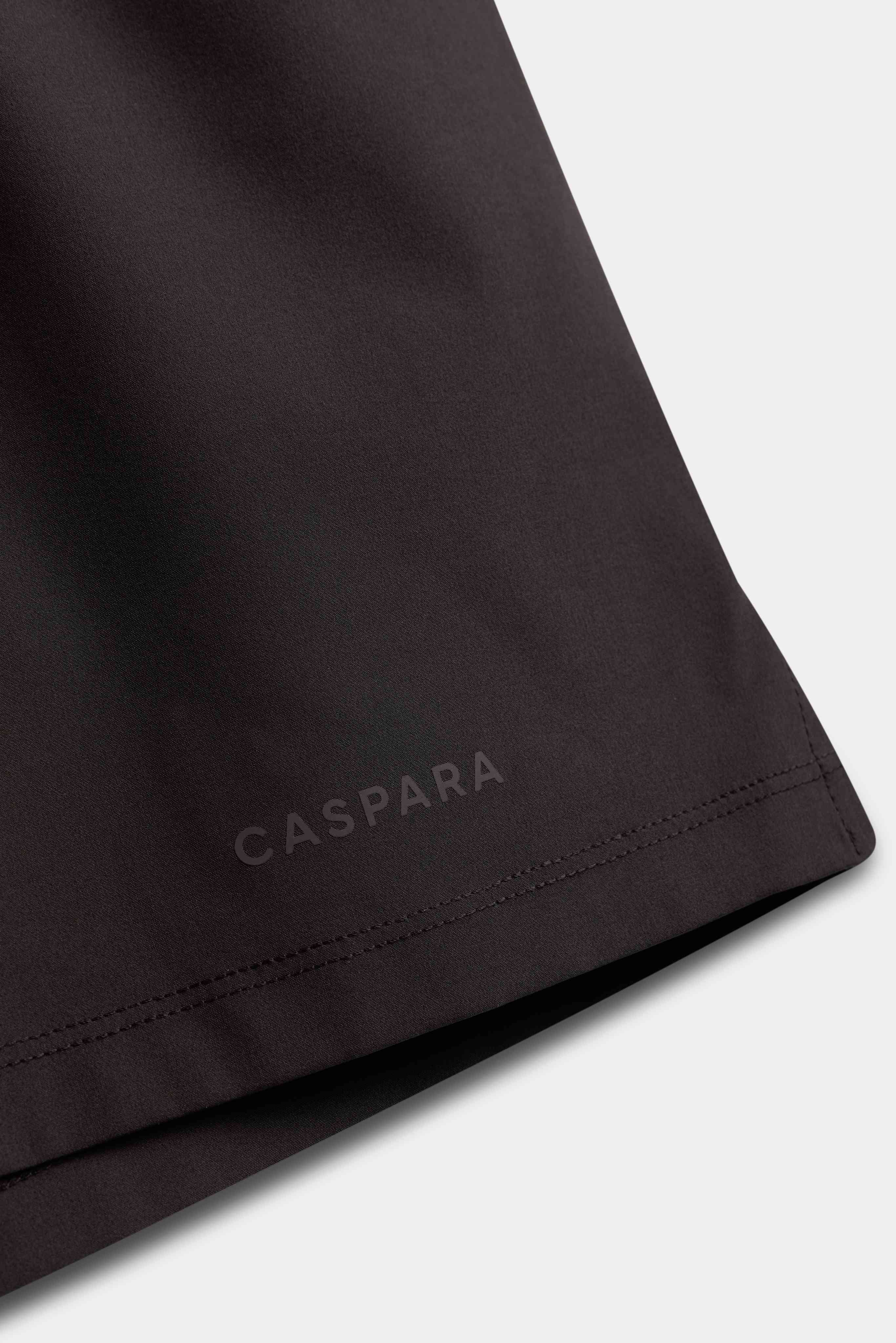 Close-up of the subtle CASPARA logo near the hem of espresso Vantage shorts.
