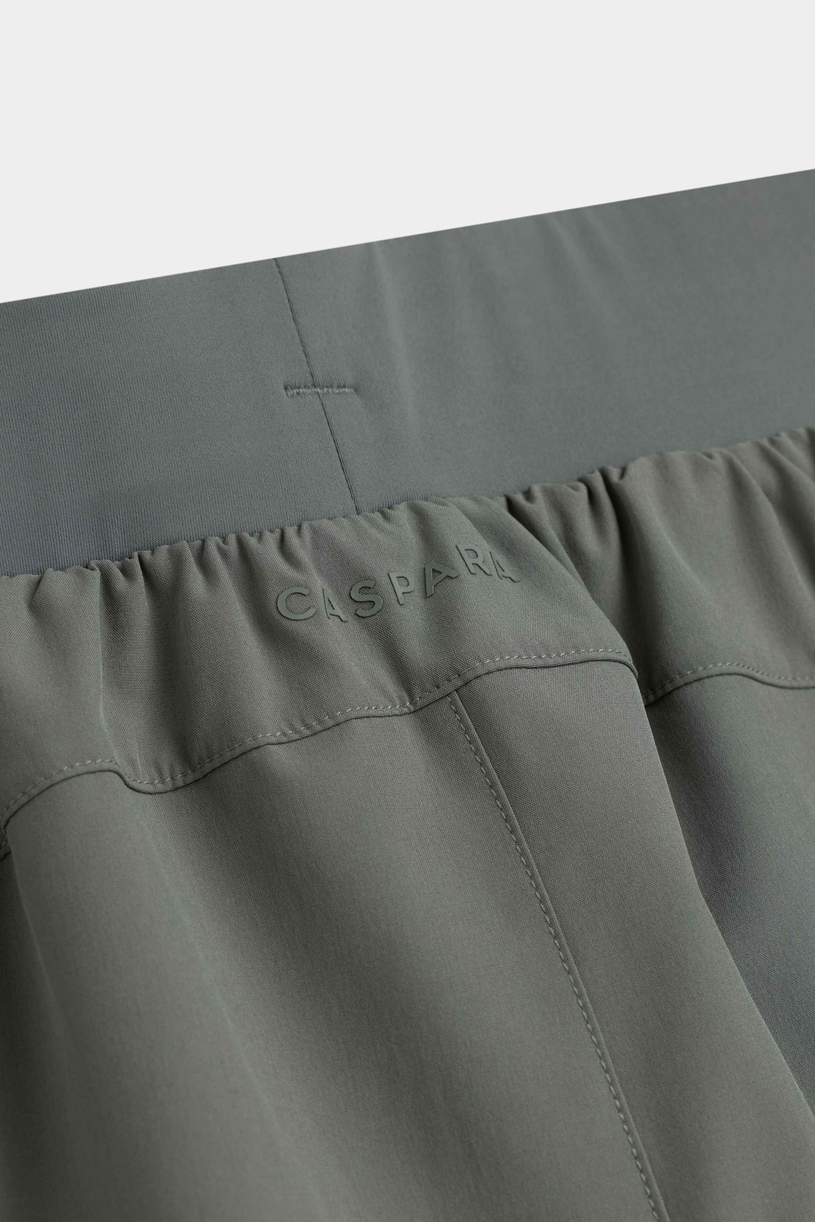 Detail view of the waistband and tonal CASPARA logo on khaki Aerluxe shorts.