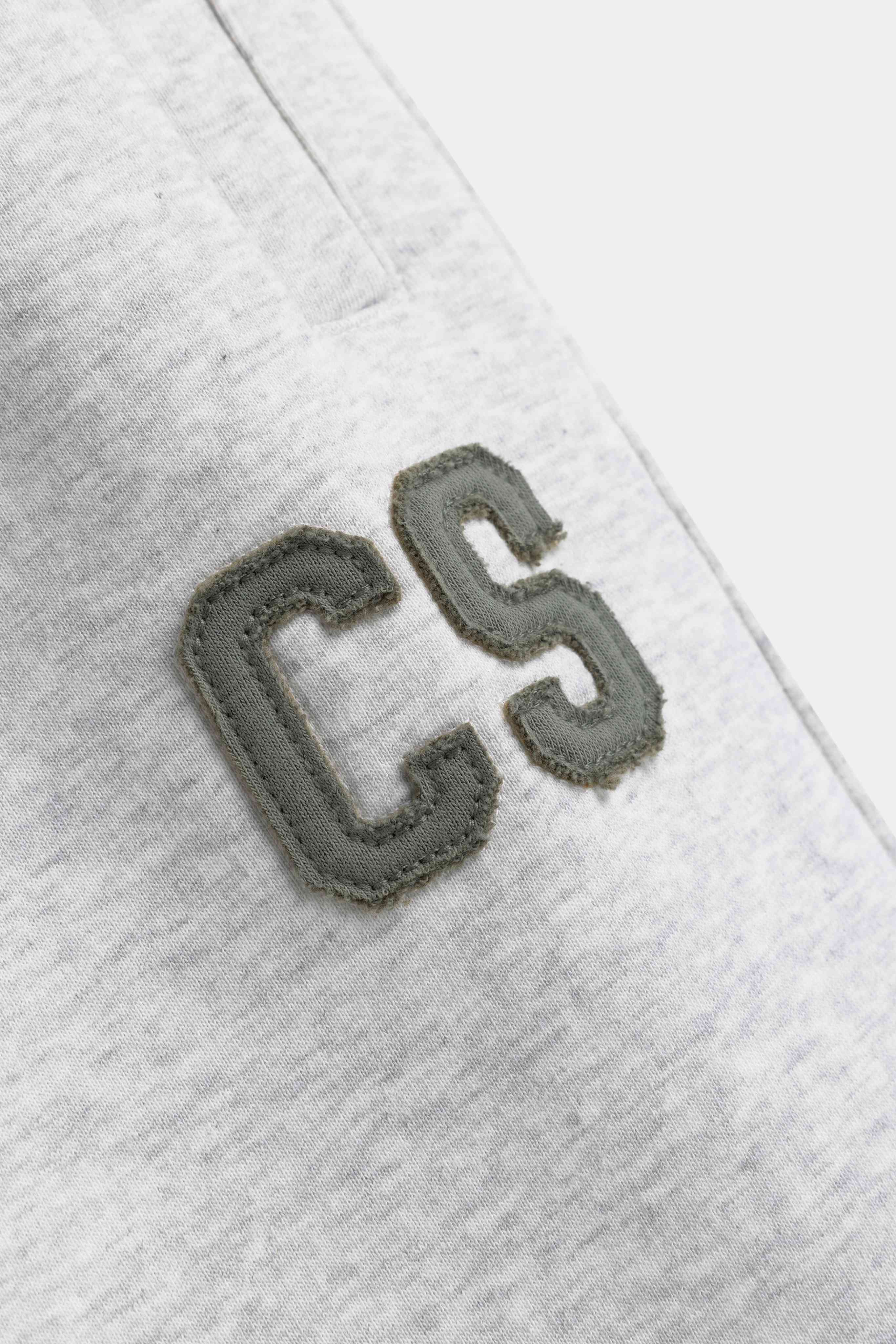 Close-up of the khaki CS logo patch on grey melange CASPARA sweatpants.