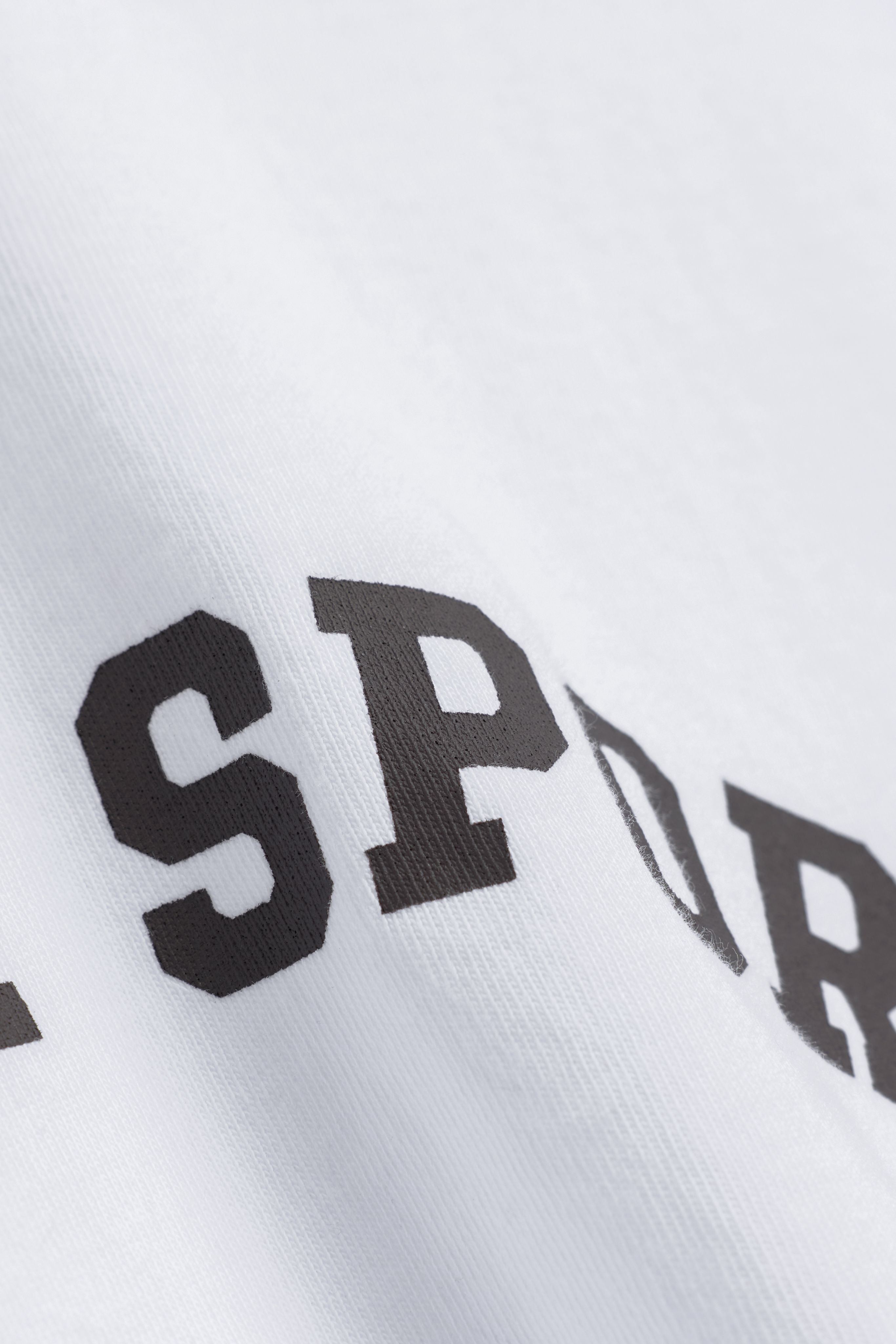 Close-up of espresso lettering printed on the white CASPARA CS Signature long sleeve.