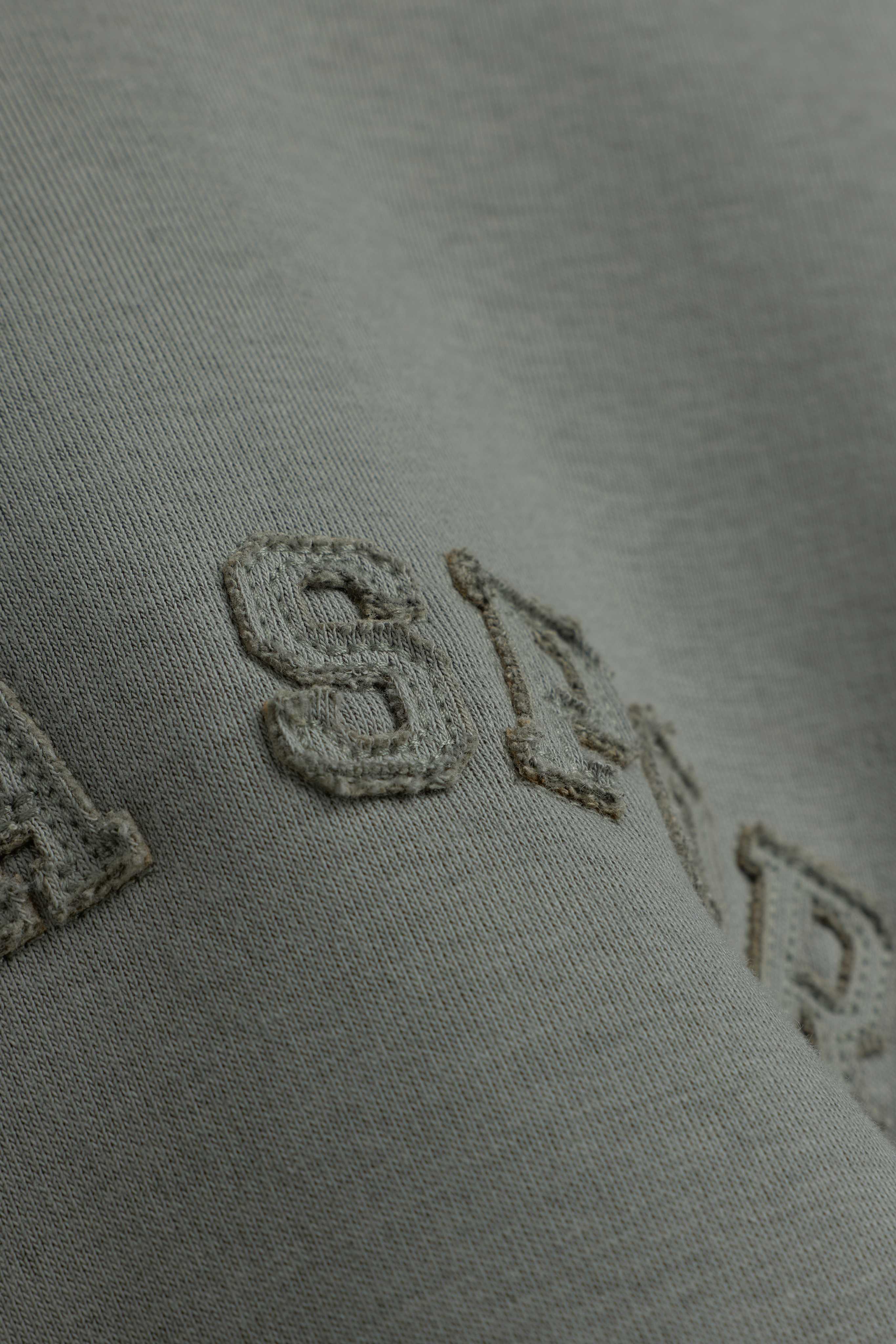 Close-up of embroidered lettering on the khaki CASPARA CS crewneck sweatshirt.