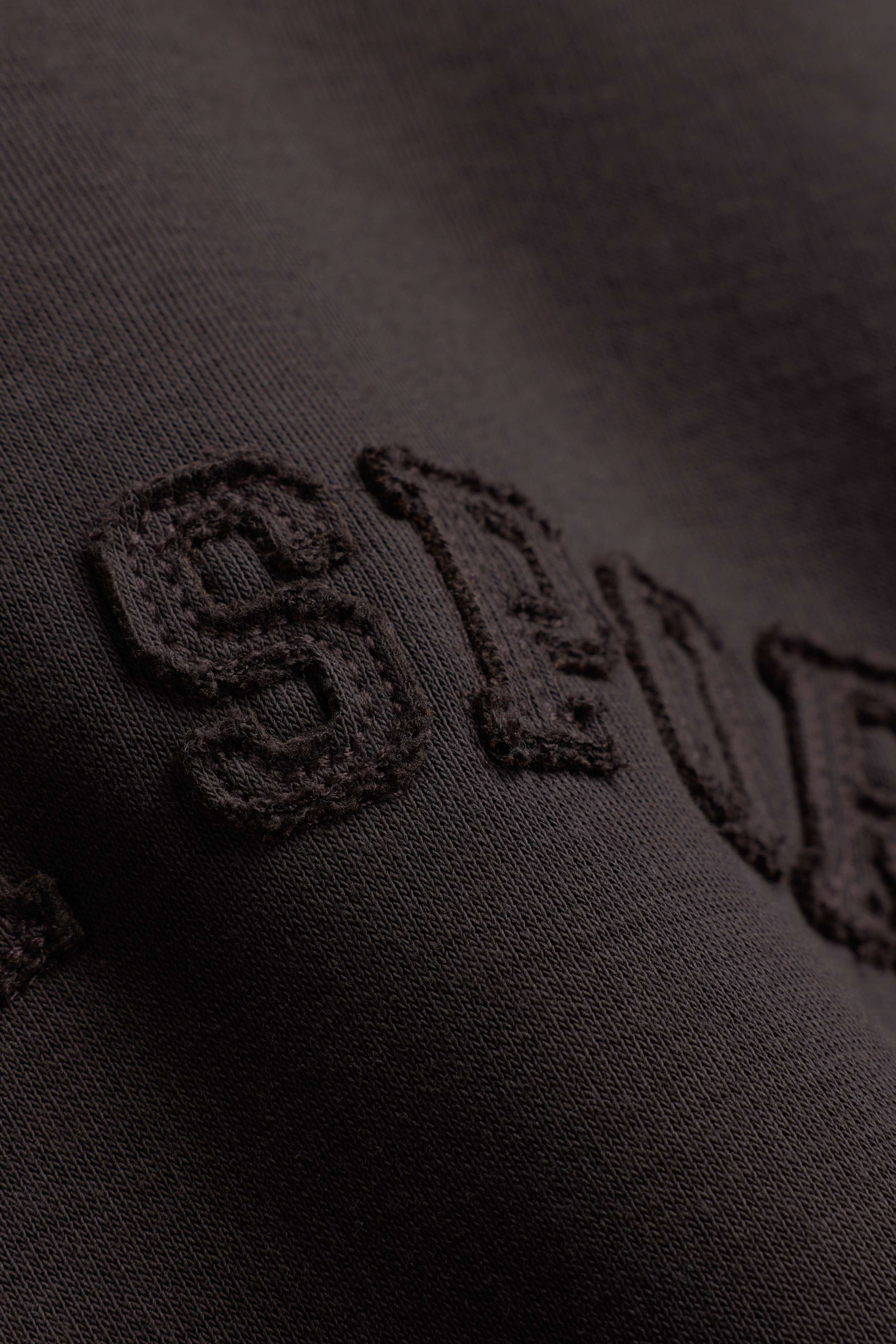 Close-up detail of the embroidered lettering on an espresso CASPARA CS crewneck sweatshirt.