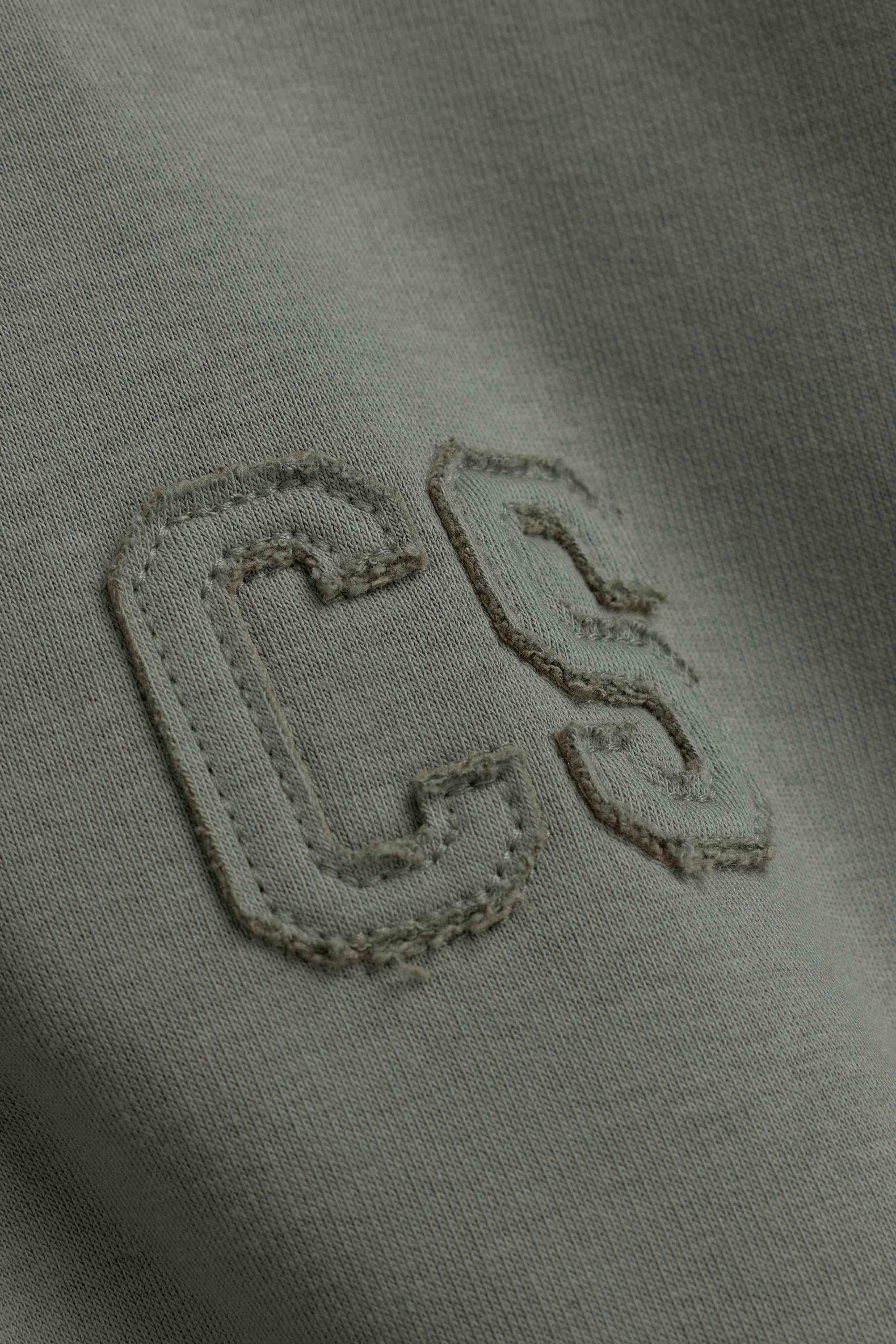 Close-up of the stitched CS logo on a khaki CASPARA CS rugby shirt.