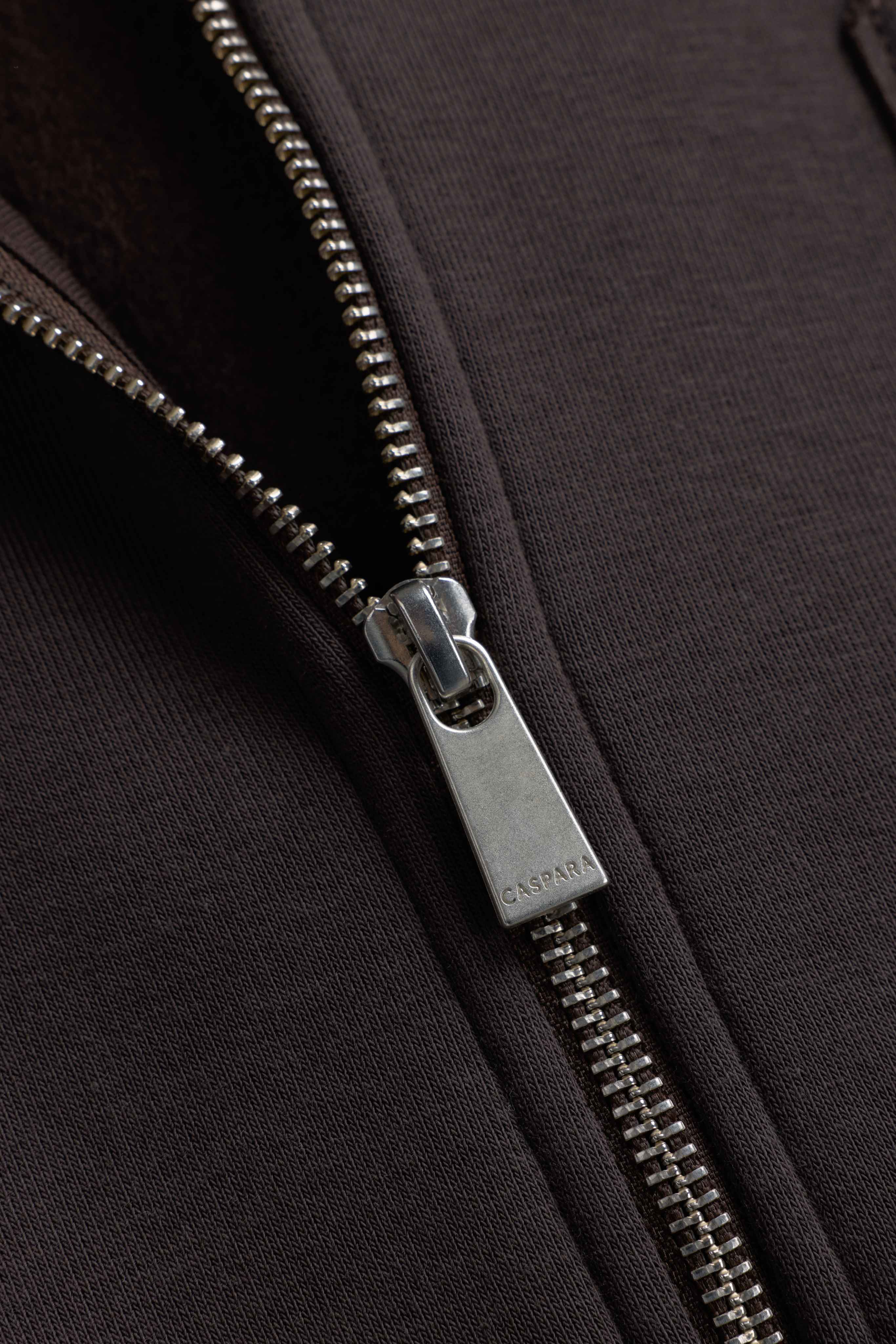Close-up of the silver CASPARA zipper pull on the espresso CS Zip Hoodie.