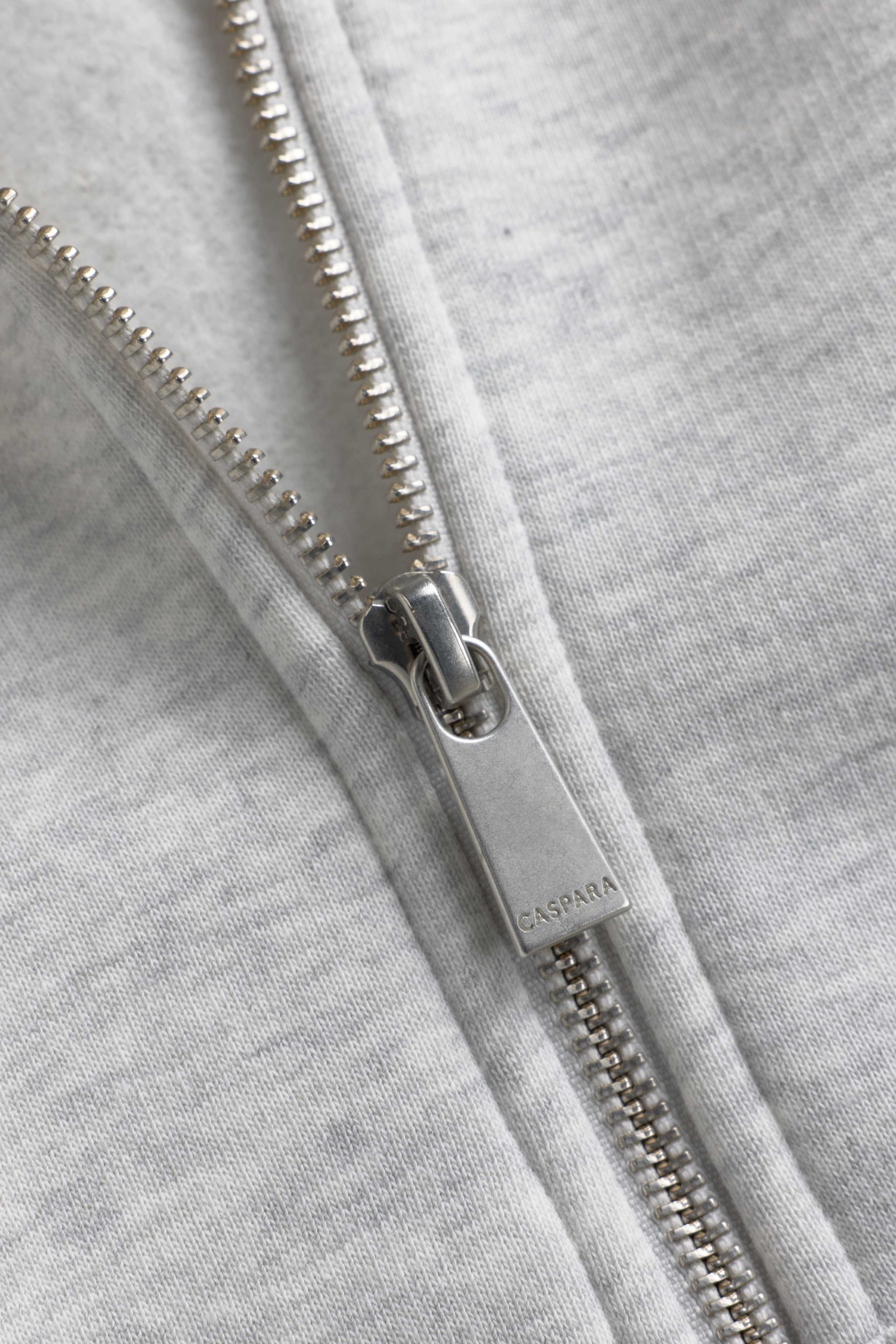 Close-up of the silver CASPARA zipper pull on a grey melange zip hoodie.