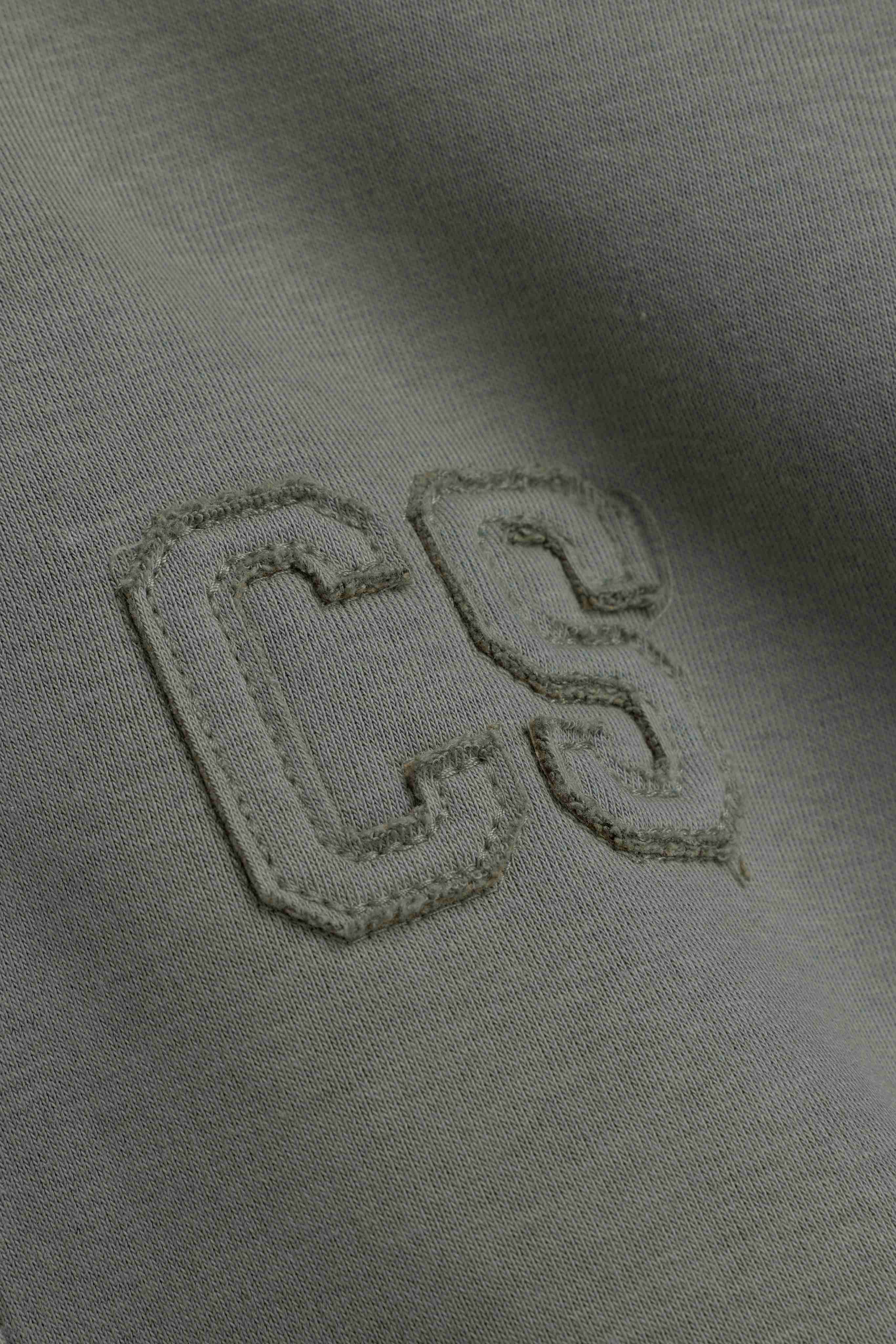 Close-up of the embroidered CS logo detail on a khaki CASPARA hoodie.
