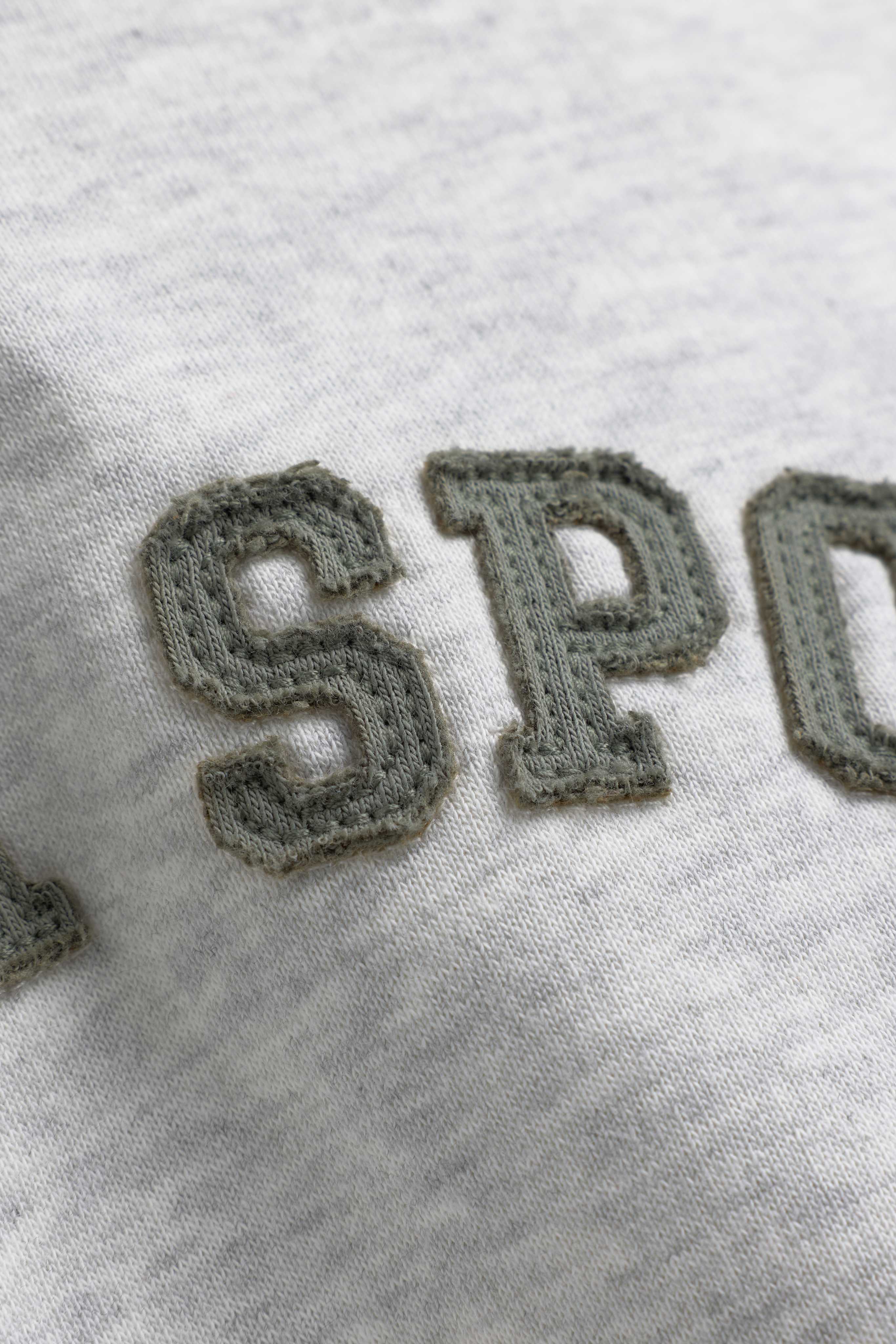 Close-up of khaki embroidered lettering on a grey melange CASPARA hoodie fabric.