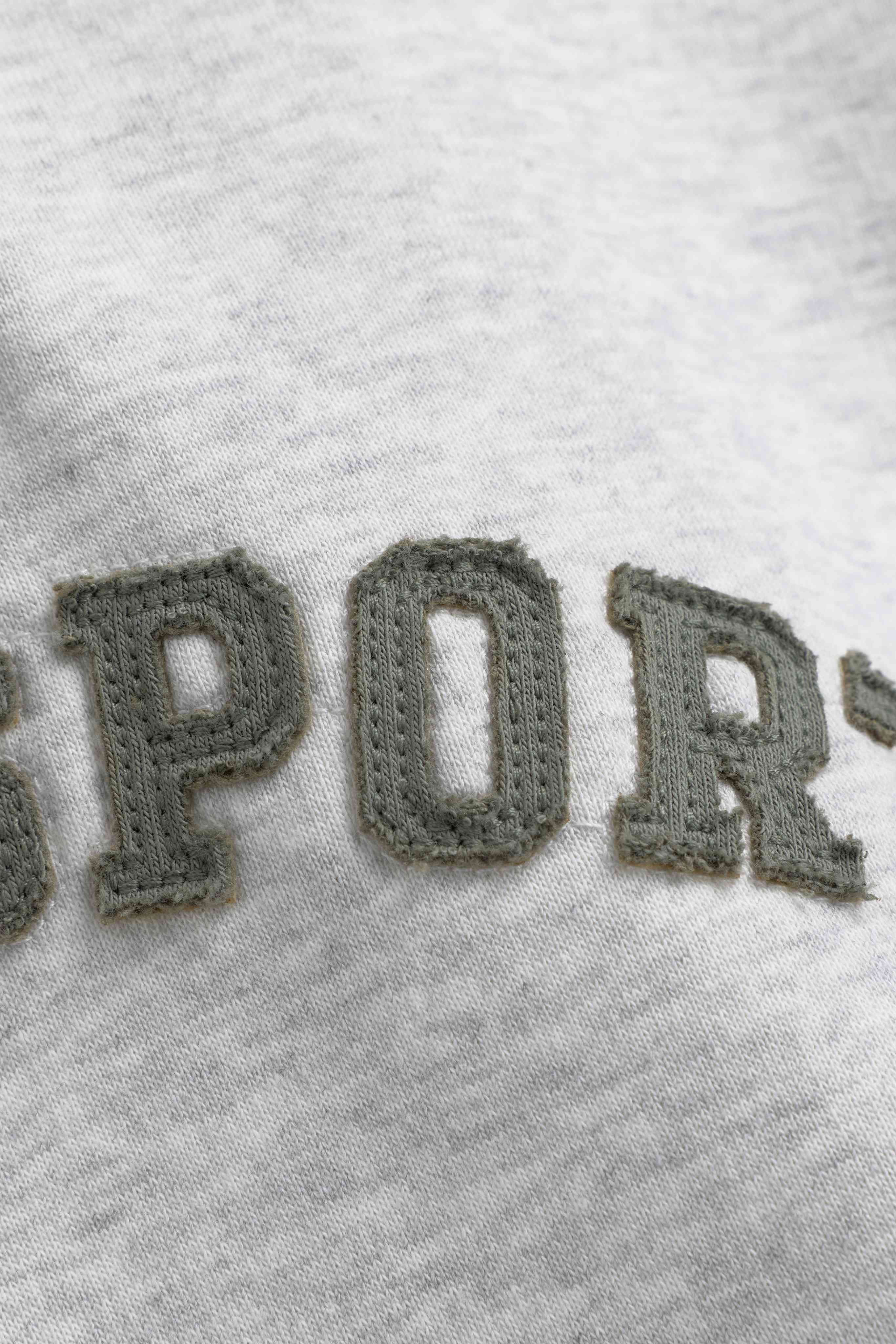 Close-up of khaki embroidered lettering on a grey melange CASPARA CS hoodie.