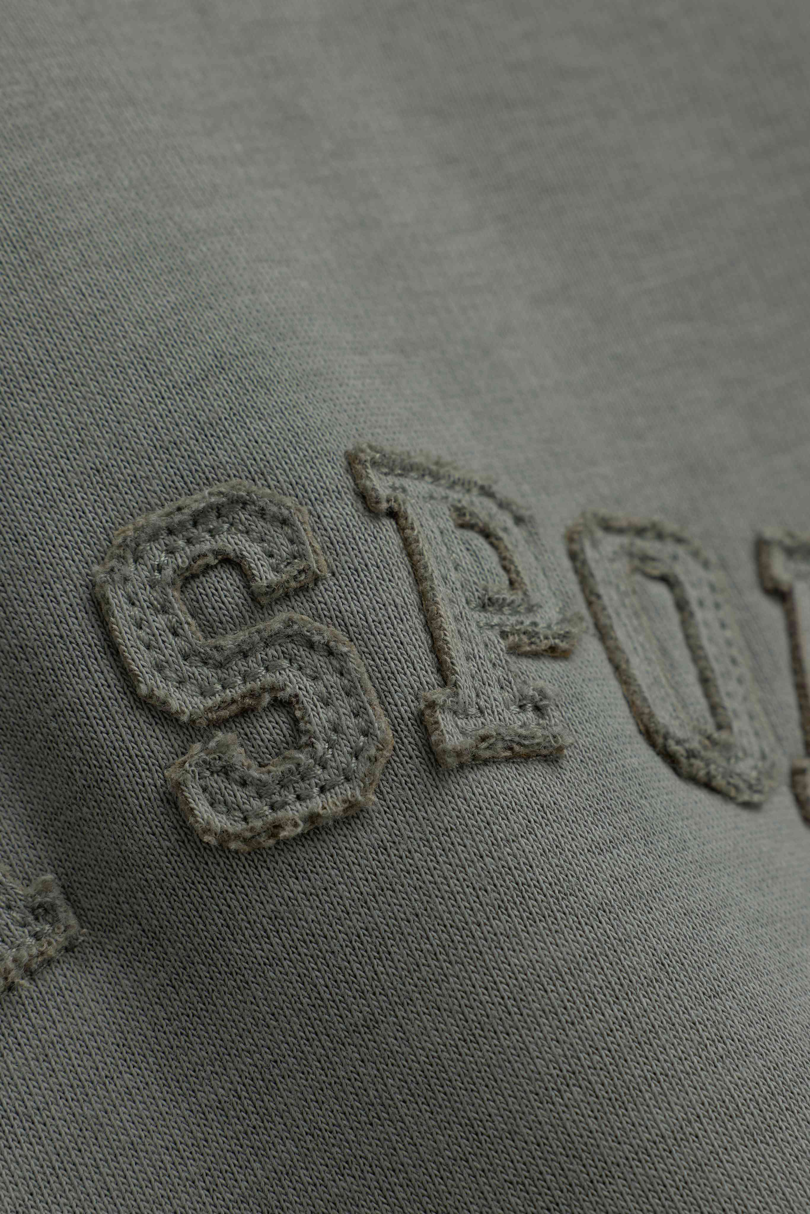 Close-up of textured embroidered lettering on the khaki CASPARA CS hoodie.