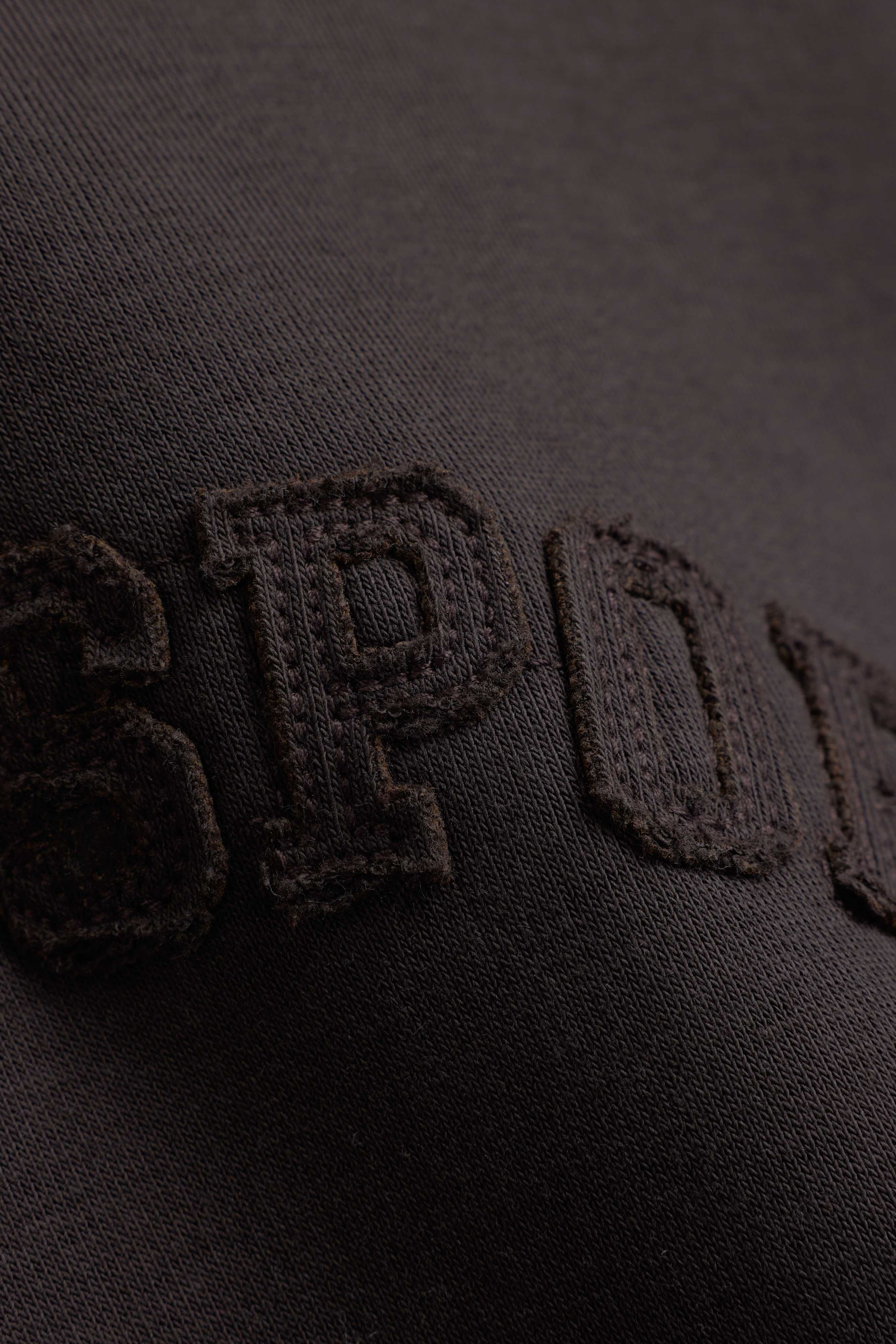 Close-up of embroidered lettering on an espresso CASPARA CS hoodie.