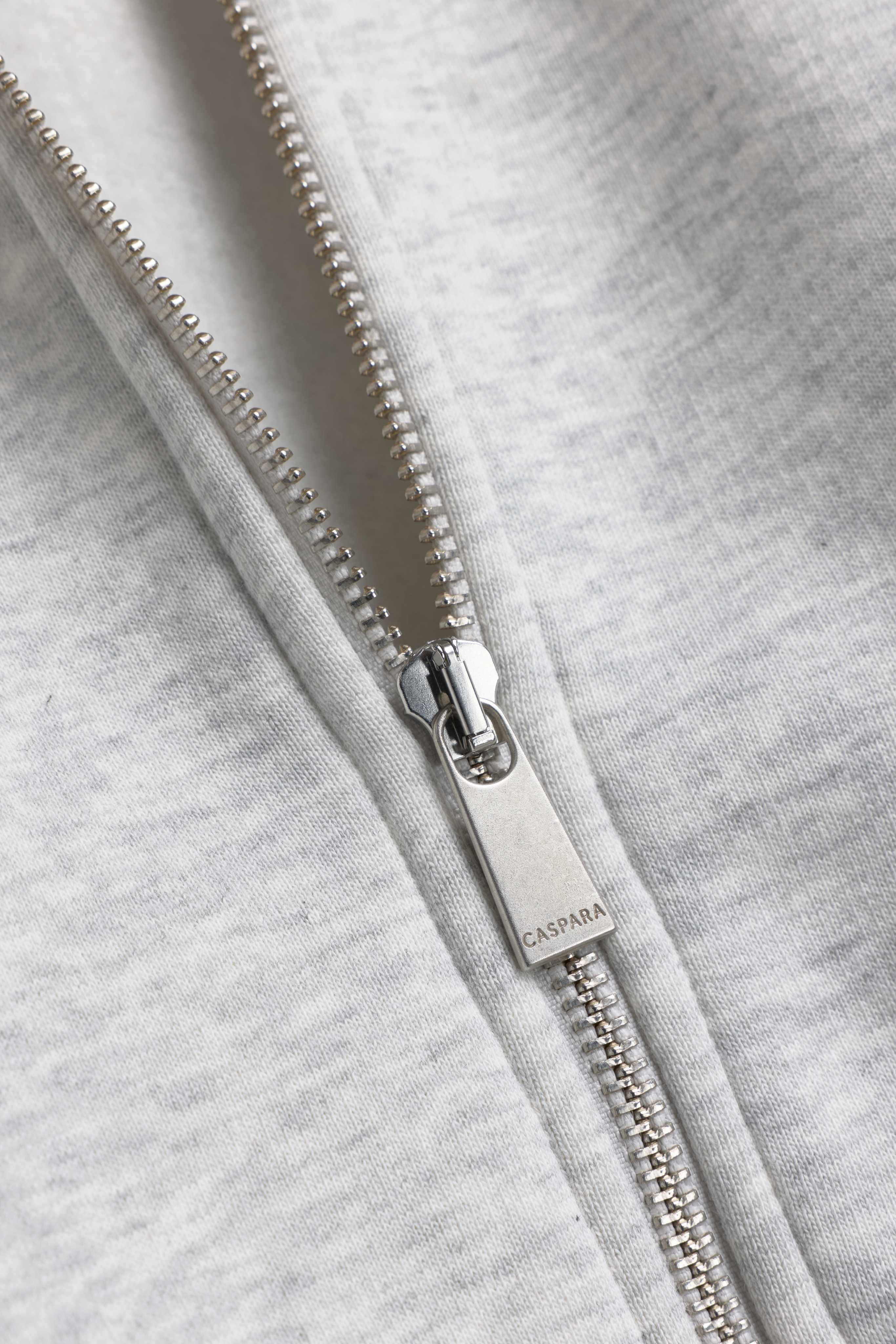 Close-up of the engraved silver zipper pull on a grey melange CASPARA hoodie.