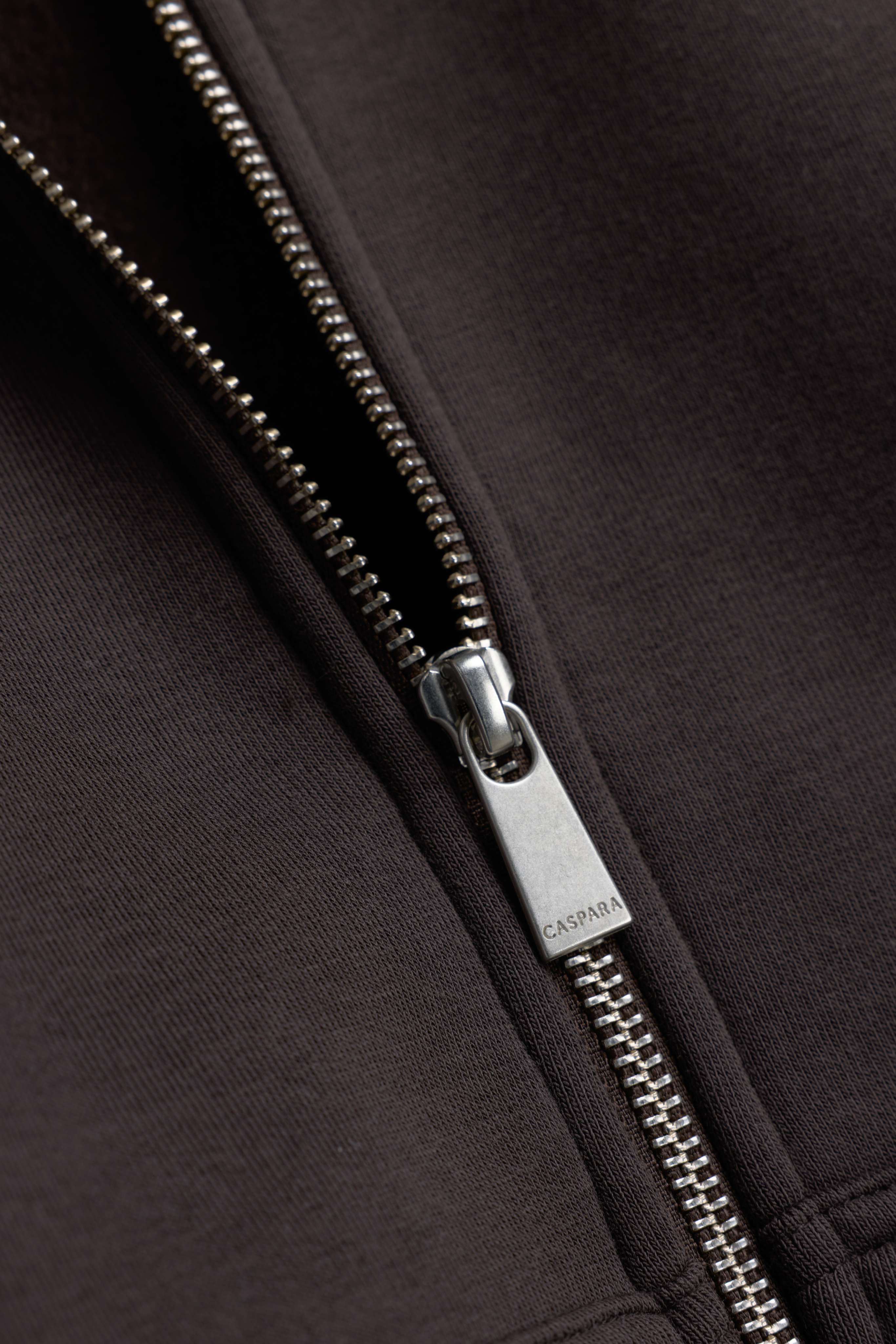 Close-up of the silver zipper pull on an espresso CASPARA CS Zip Hoodie.