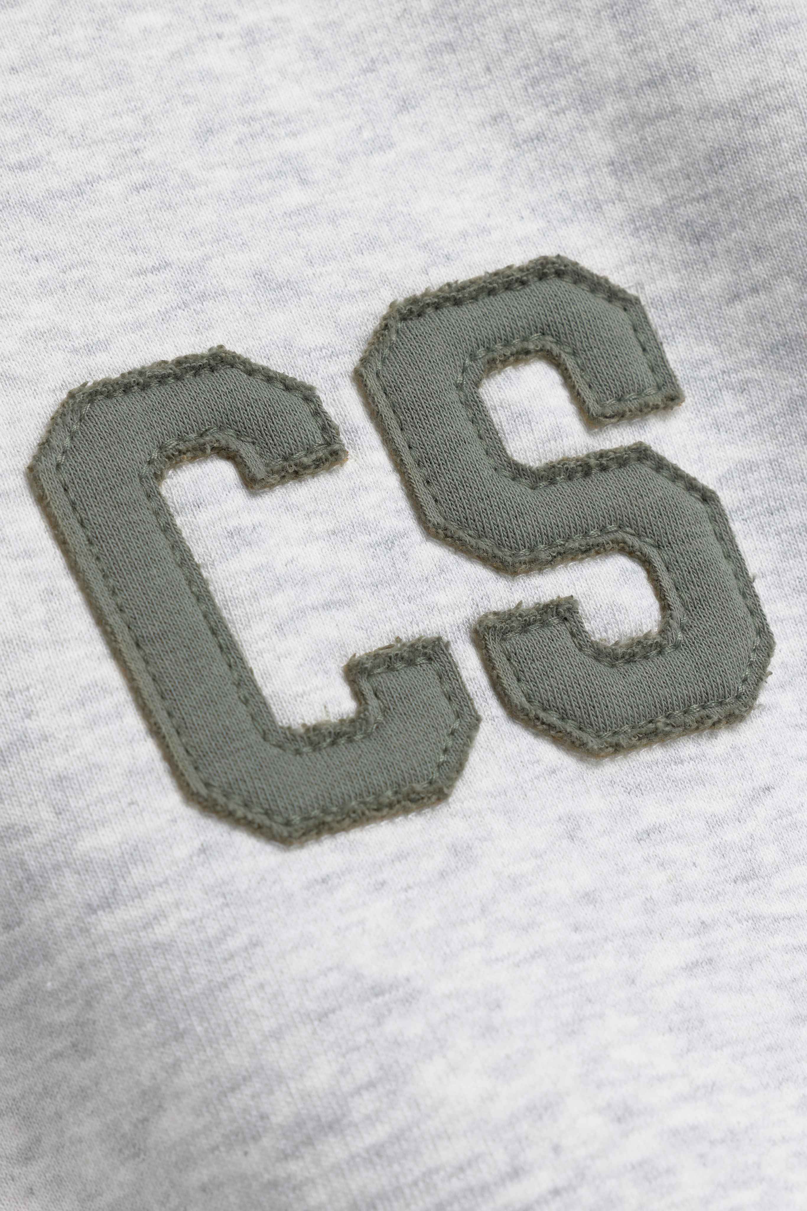 Close-up of stitched khaki CS lettering on a grey melange CASPARA rugby shirt.