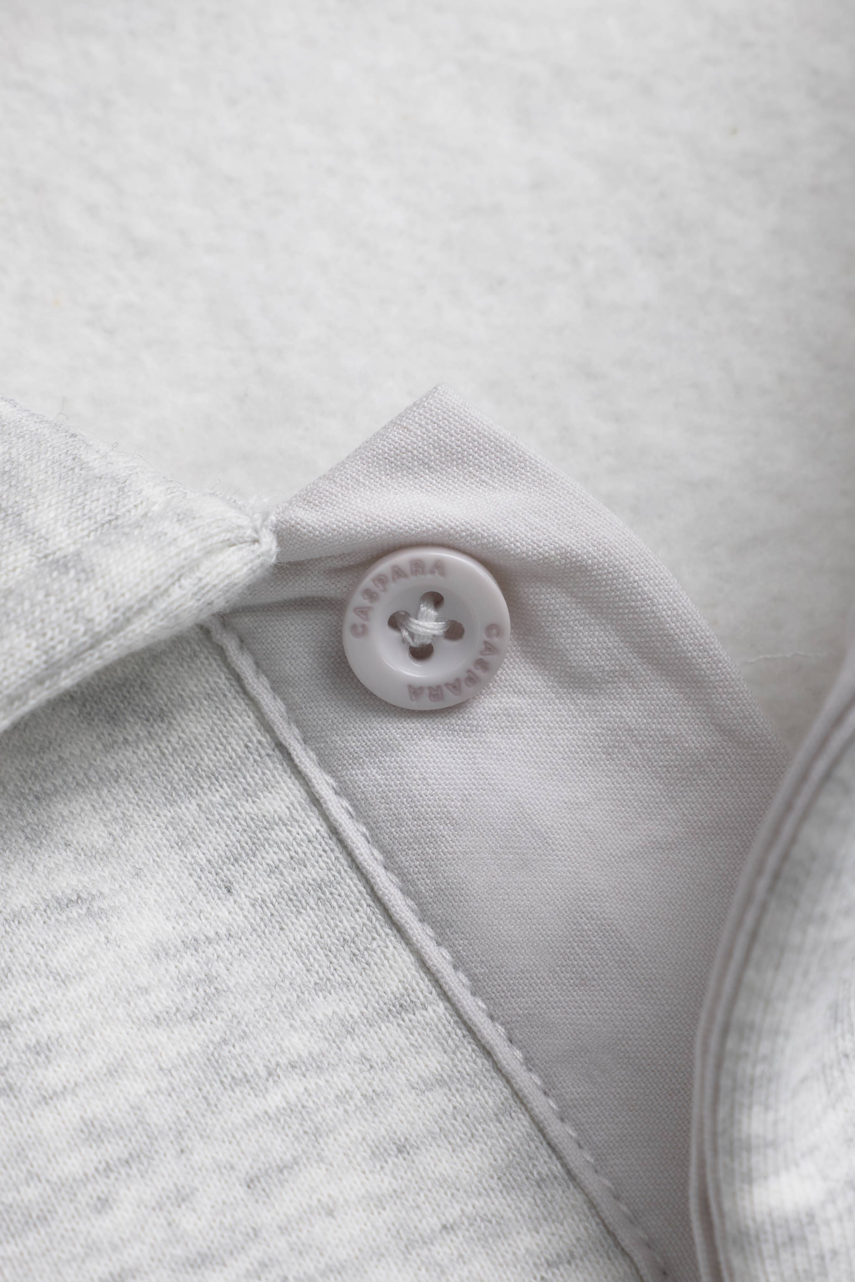 Close-up of the engraved button and placket on a grey melange CASPARA CS rugby shirt.