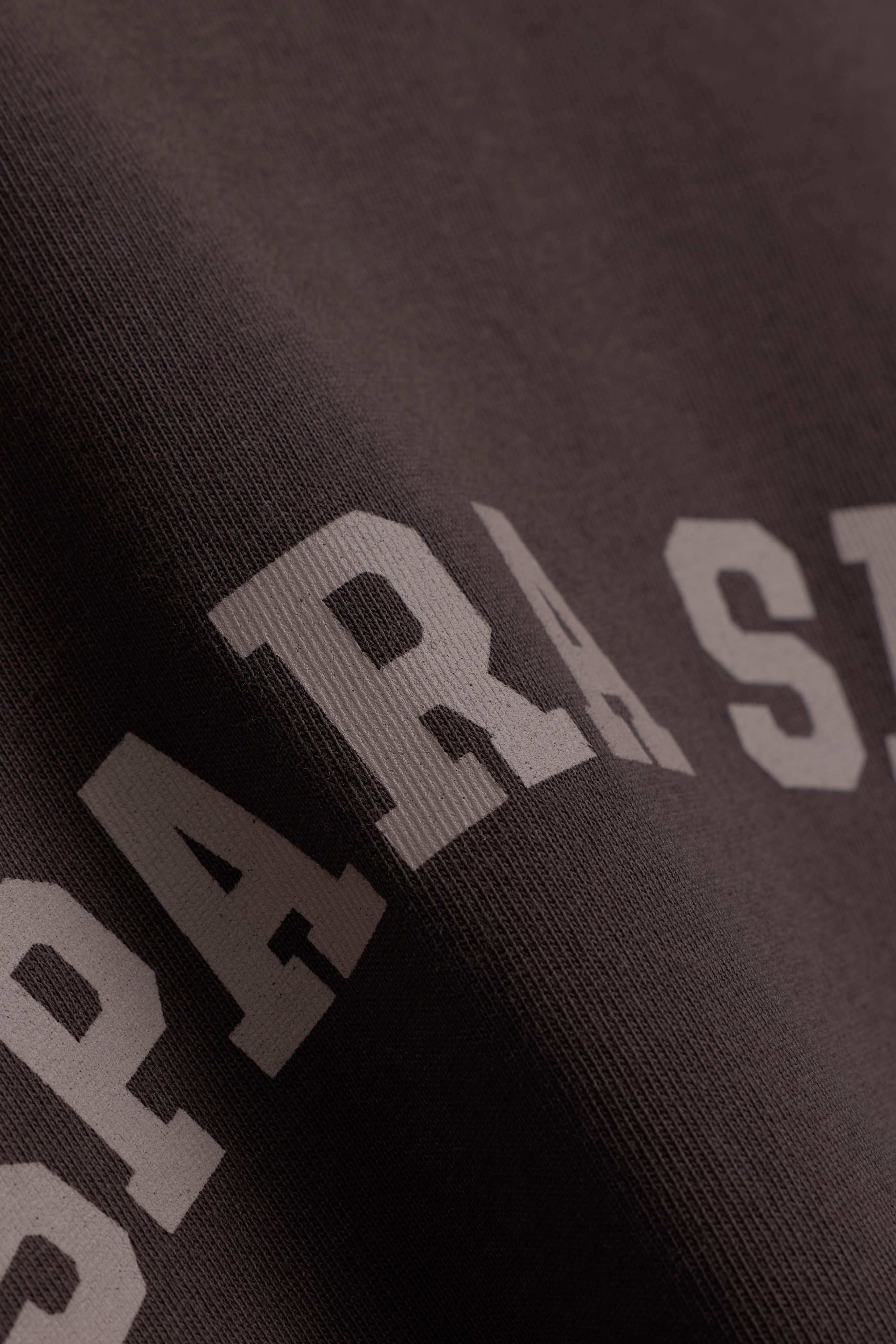 Close-up of espresso brown cotton fabric with printed lettering on the CASPARA CS Signature long sleeve.