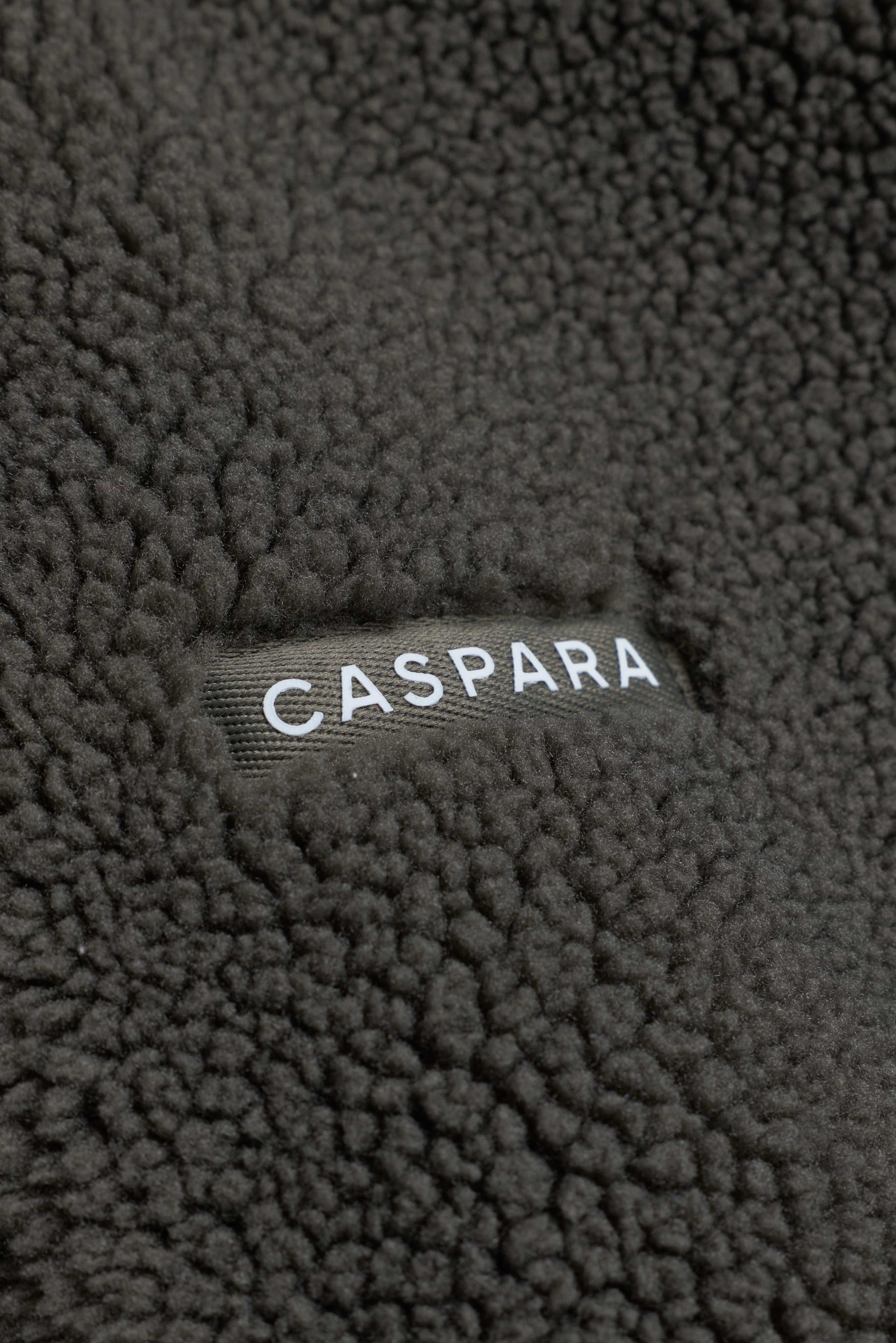 Close-up of textured khaki fleece fabric featuring a CASPARA logo label.