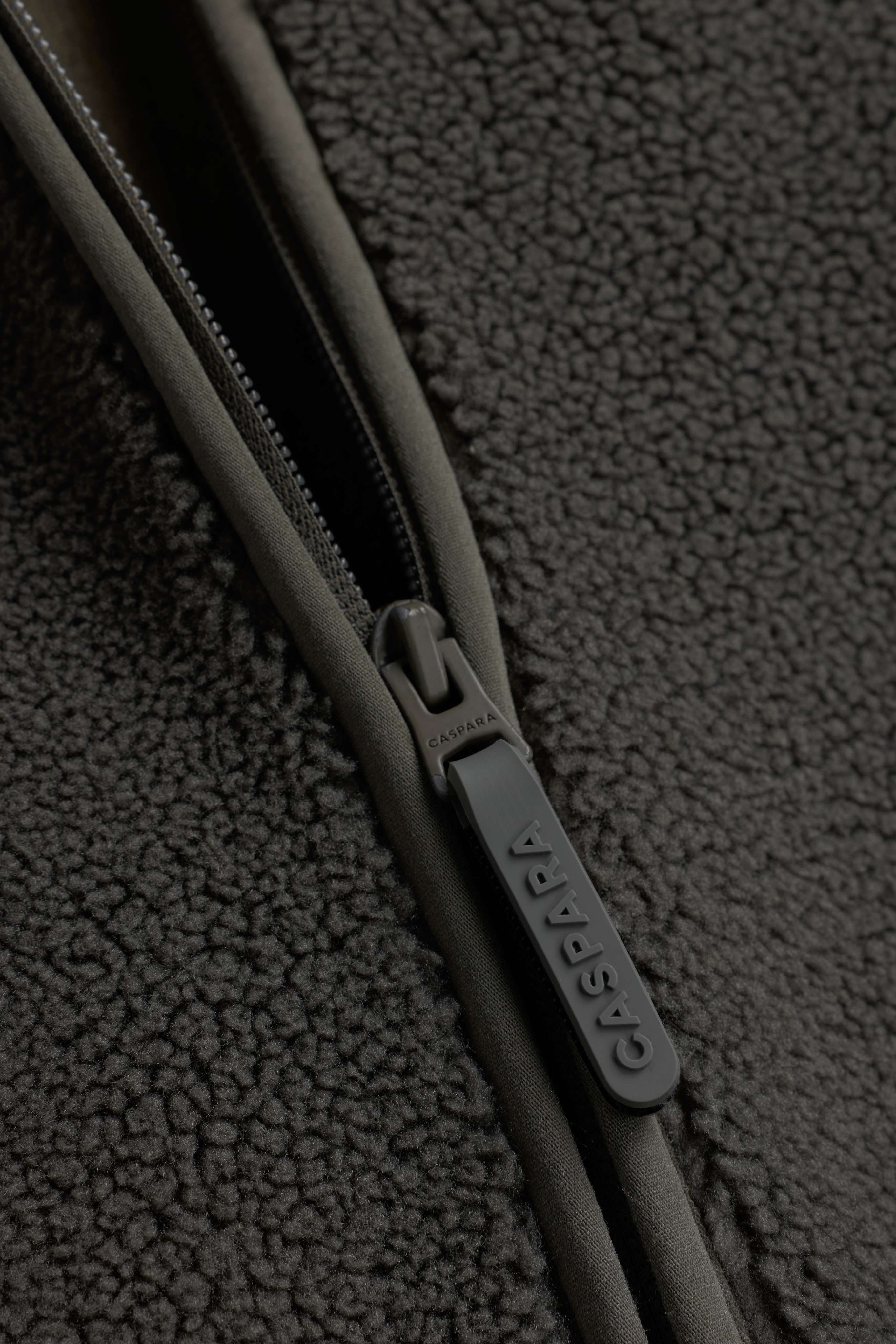 Close-up of the branded CASPARA zipper pull on the khaki Cloudfleece vest.