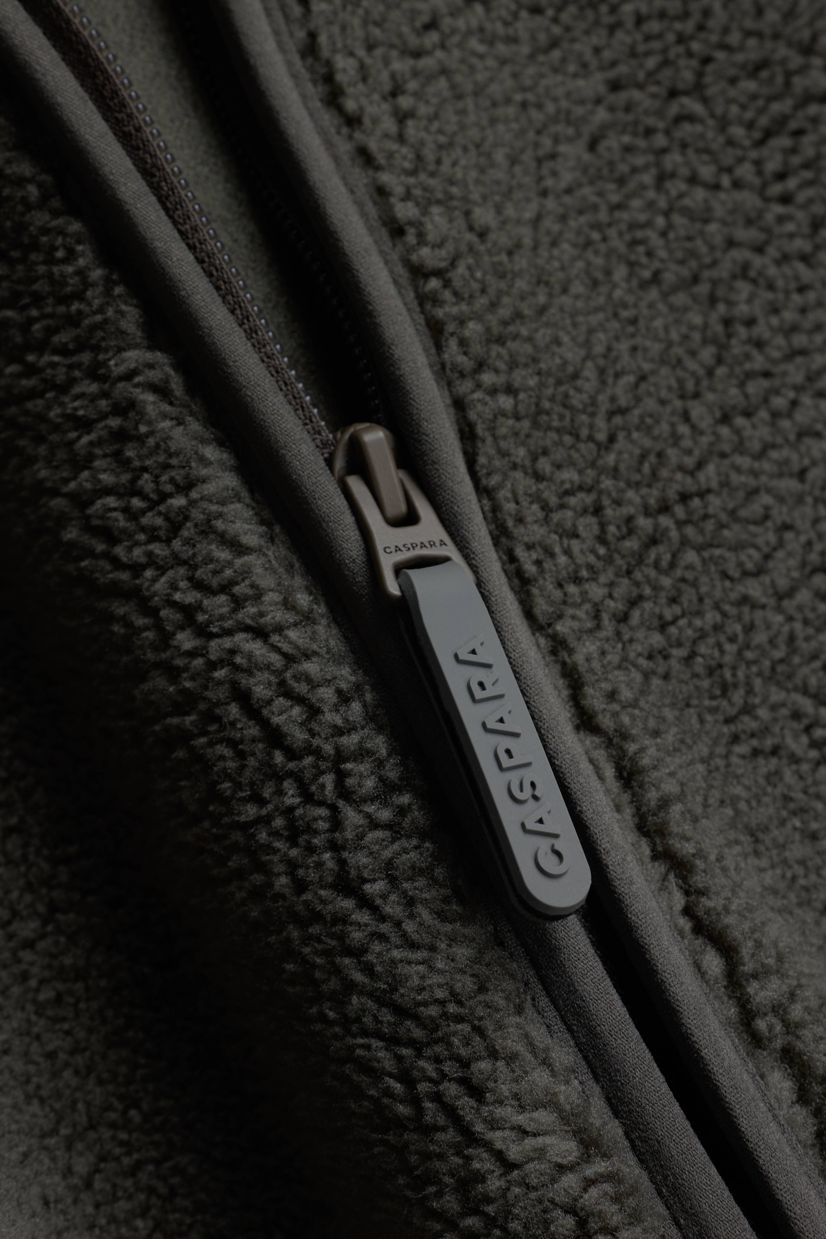 Close-up of the branded zipper pull and textured fleece on the khaki CASPARA Cloudfleece jacket.