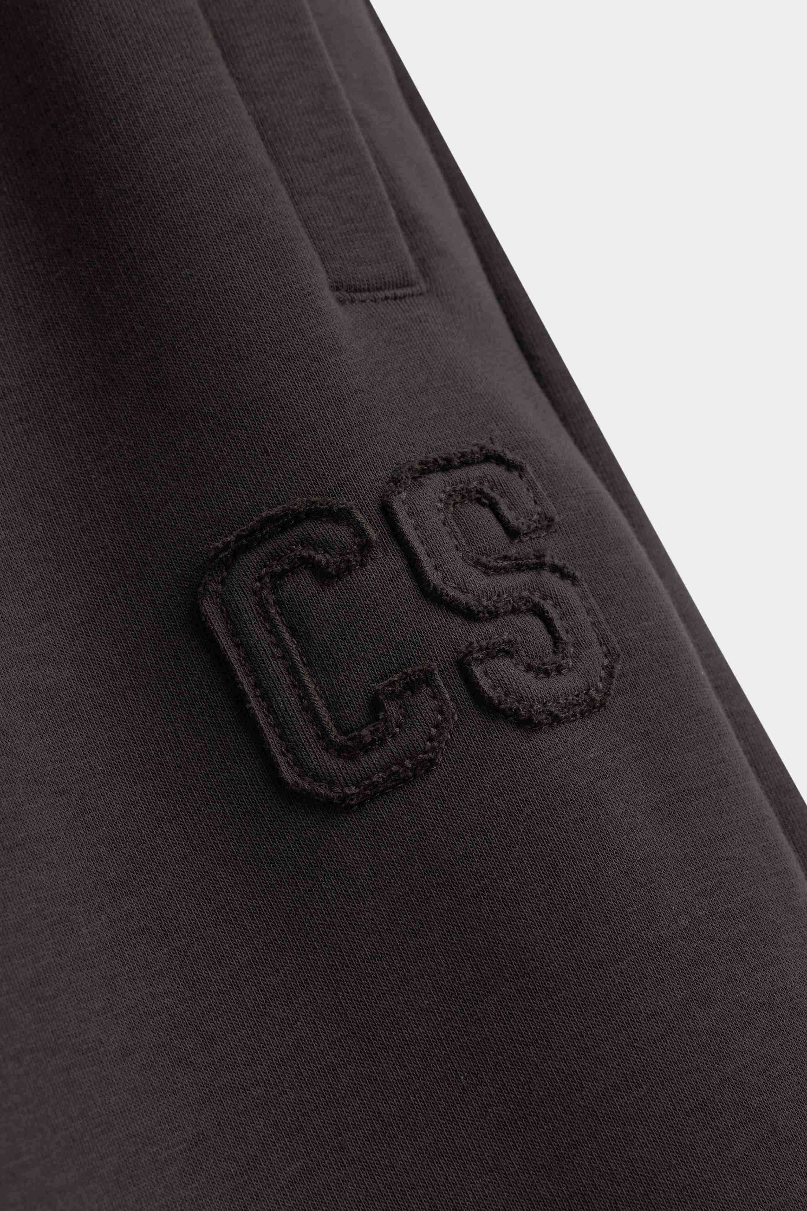 Close-up of the tonal embroidered CS logo on espresso CASPARA sweatpants.