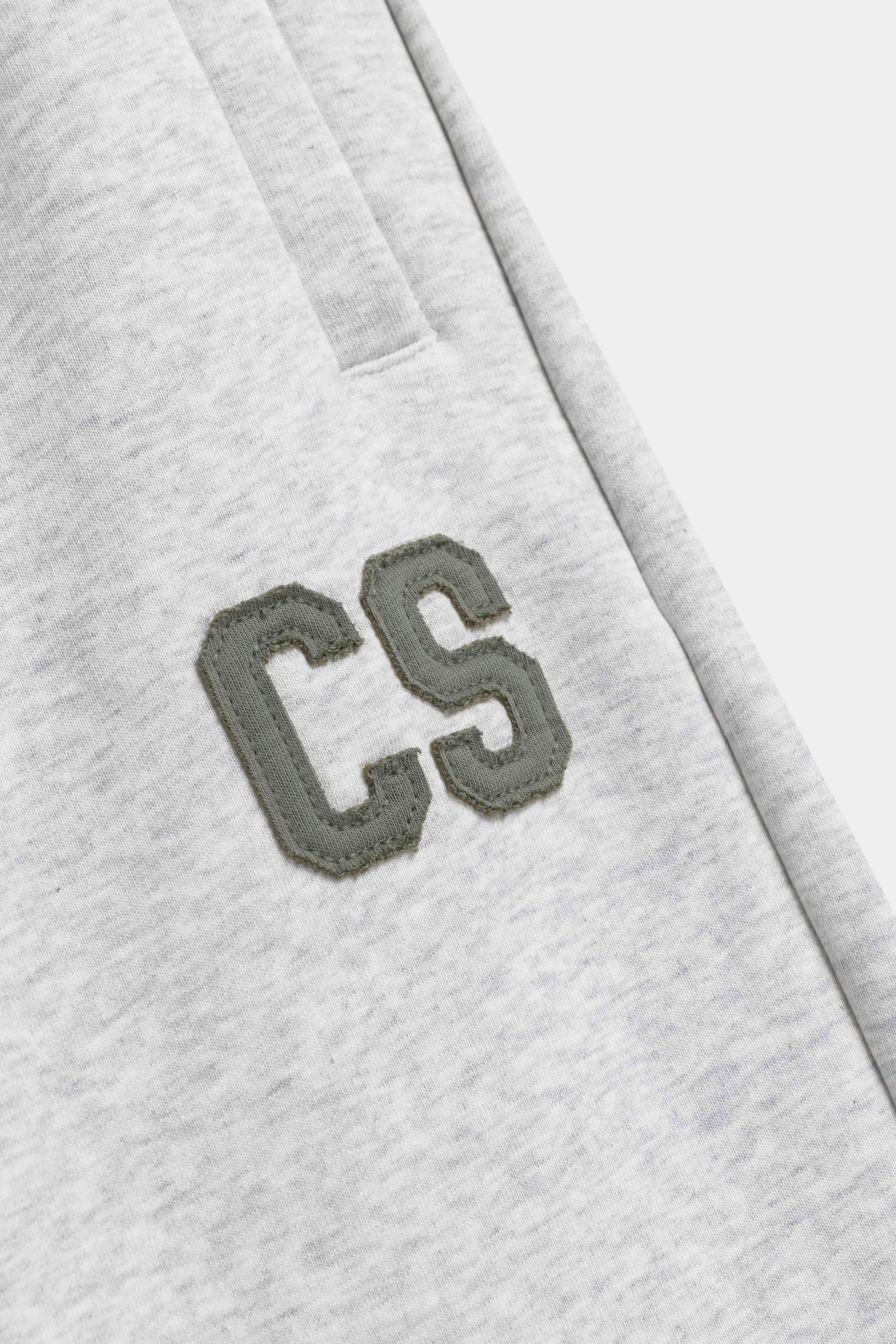 Close-up detail of the khaki embroidered CS patch on grey melange CASPARA sweatpants.